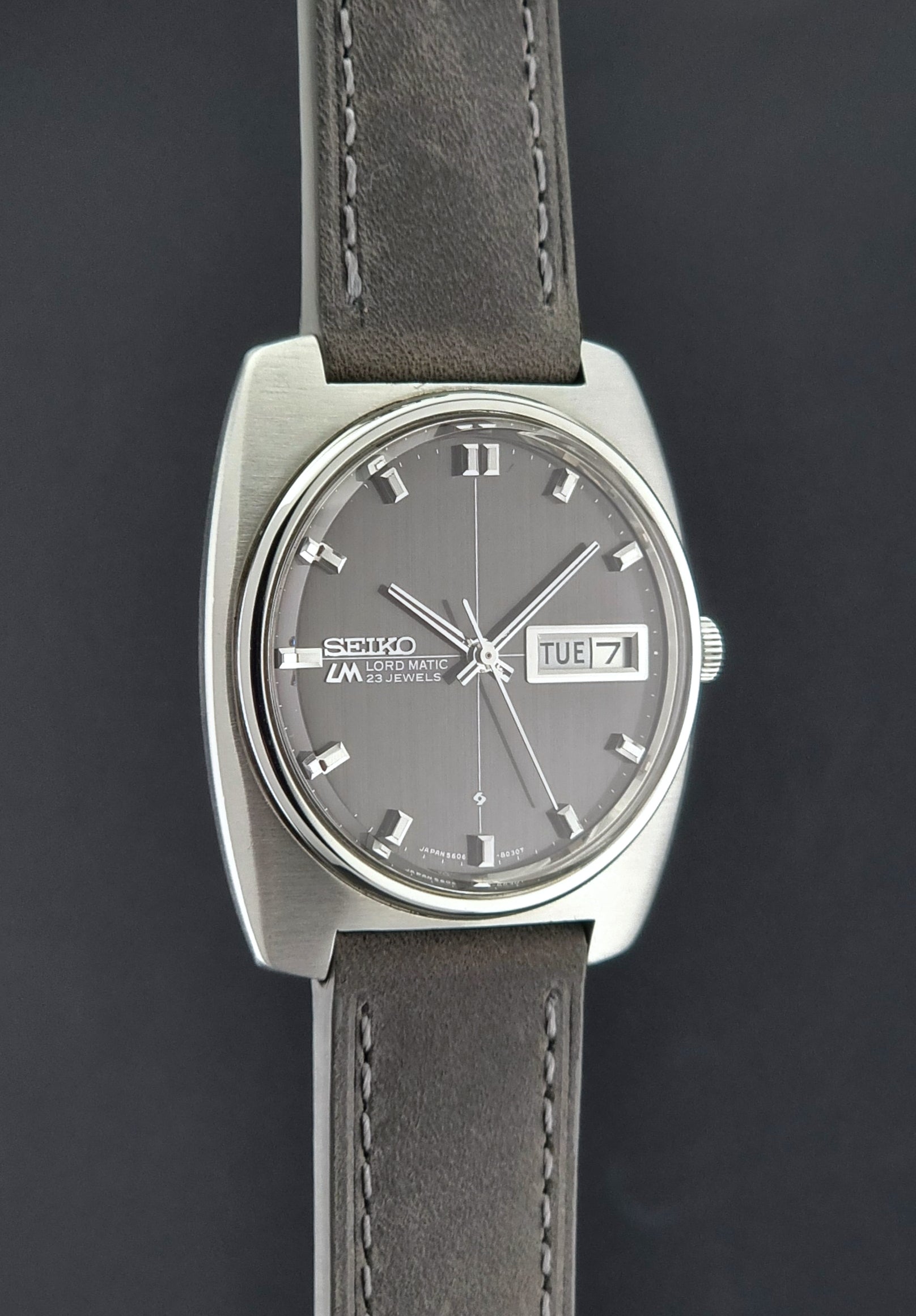 Vintage Seiko Lord Matic 5606-8010 watch with grey leather strap on a gray background side profile