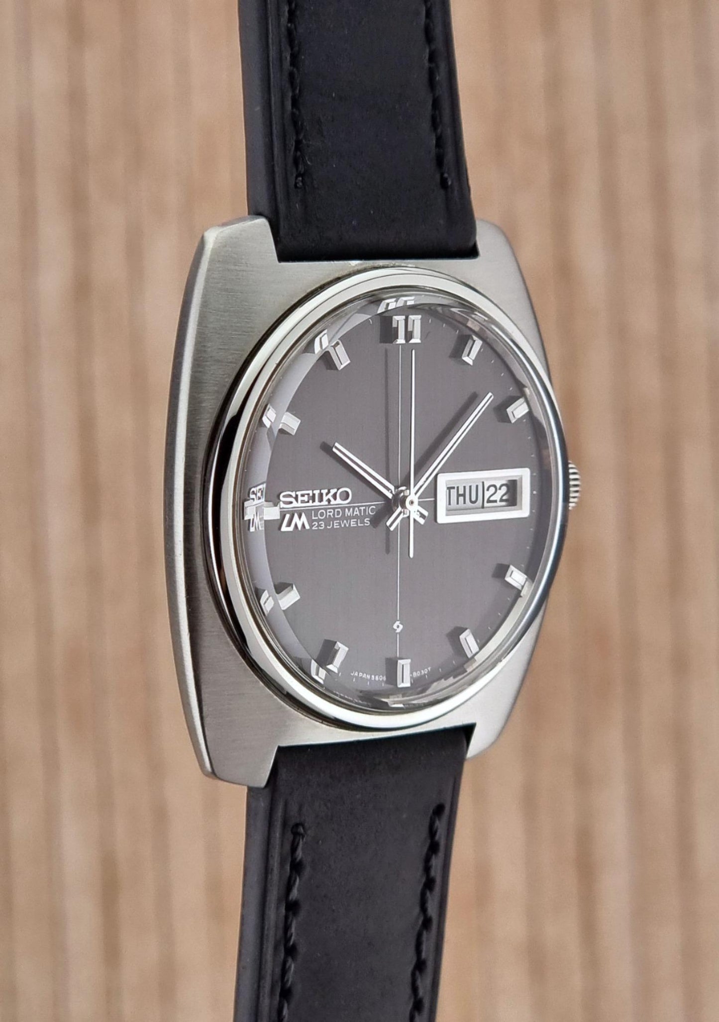 Side view of a Seiko Lord Matic watch with black strap on a wooden background