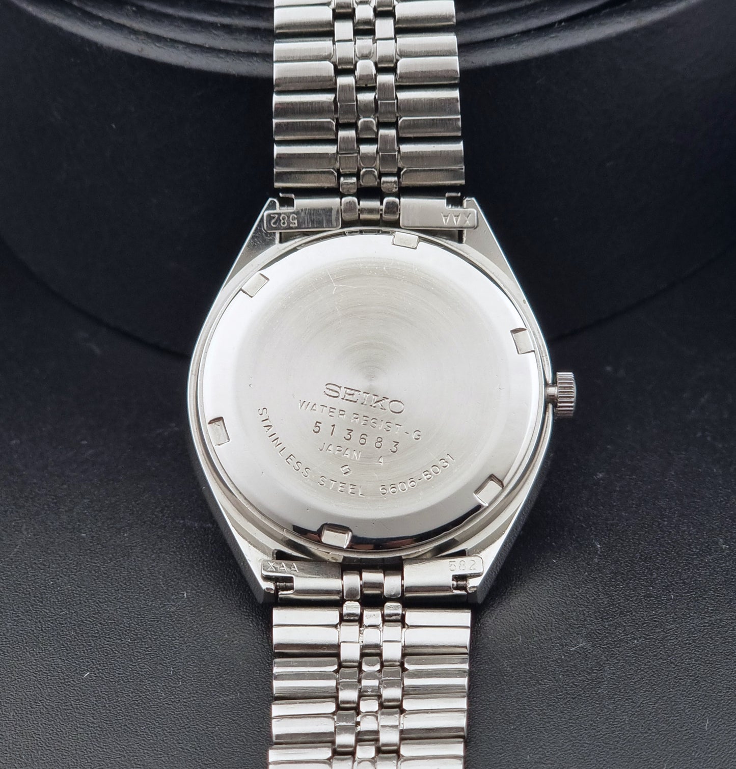 The back of a stainless steel Vintage Seiko watch LordMatic 5606-8031 with a metal link bracelet, photographed close-up against a dark textured background.