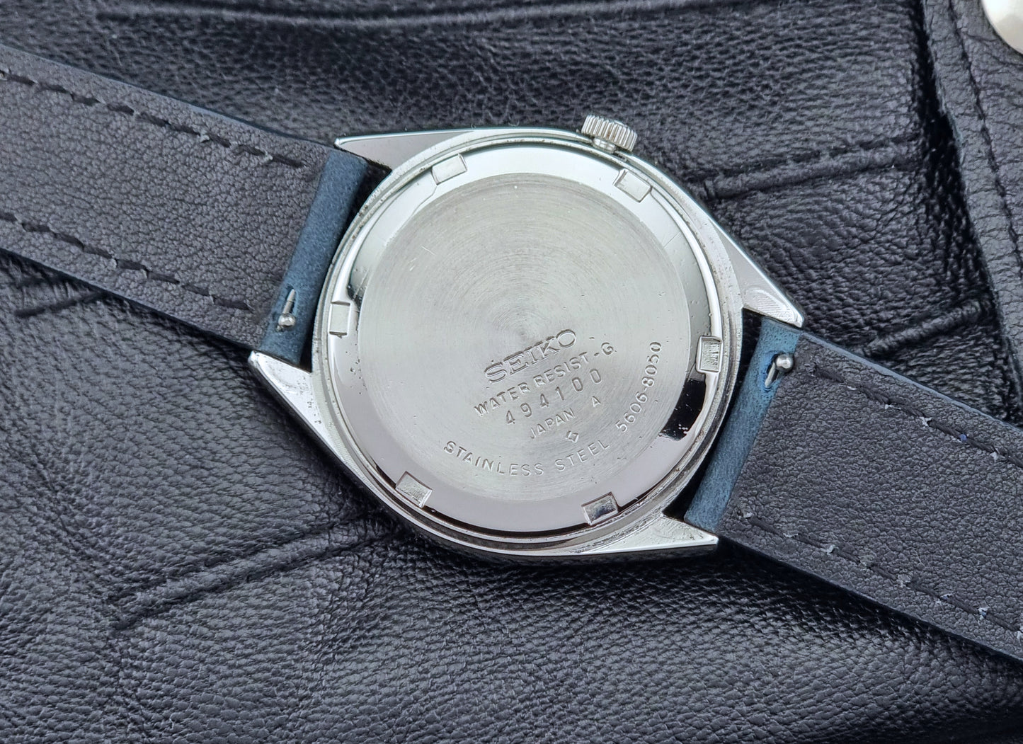 Vintage Seiko watch LordMatic 5606-8050 with blue leather strap on a dark gray background case back