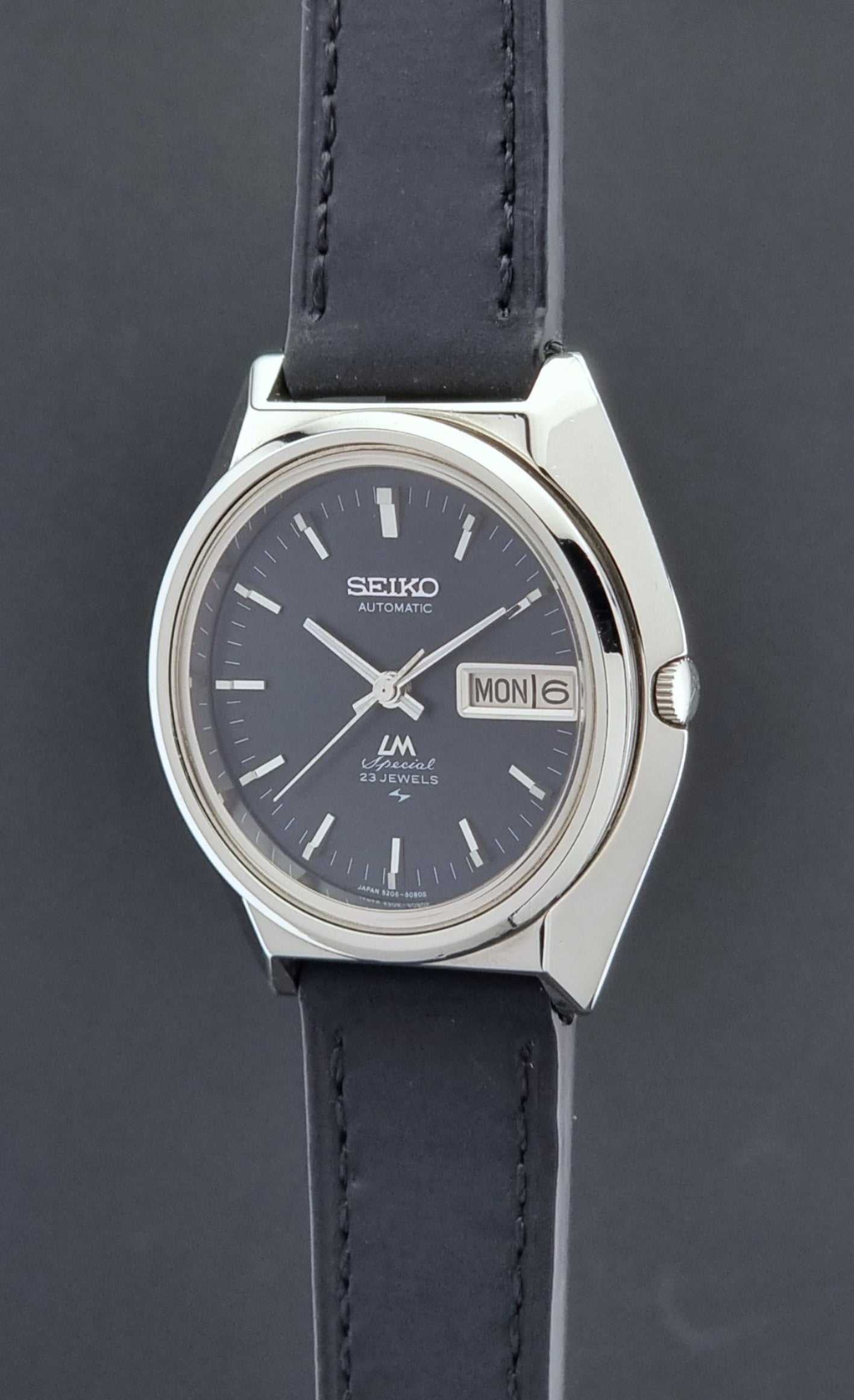 Vintage Seiko Lord Matic Special 5206-6080 watch with black leather strap on a gray background crown profile