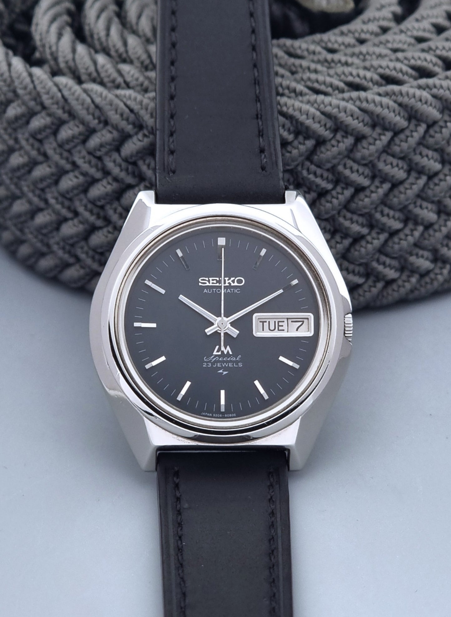 Vintage Seiko Lord Matic Special 5206-6080 watch with black leather strap on a gray background front view