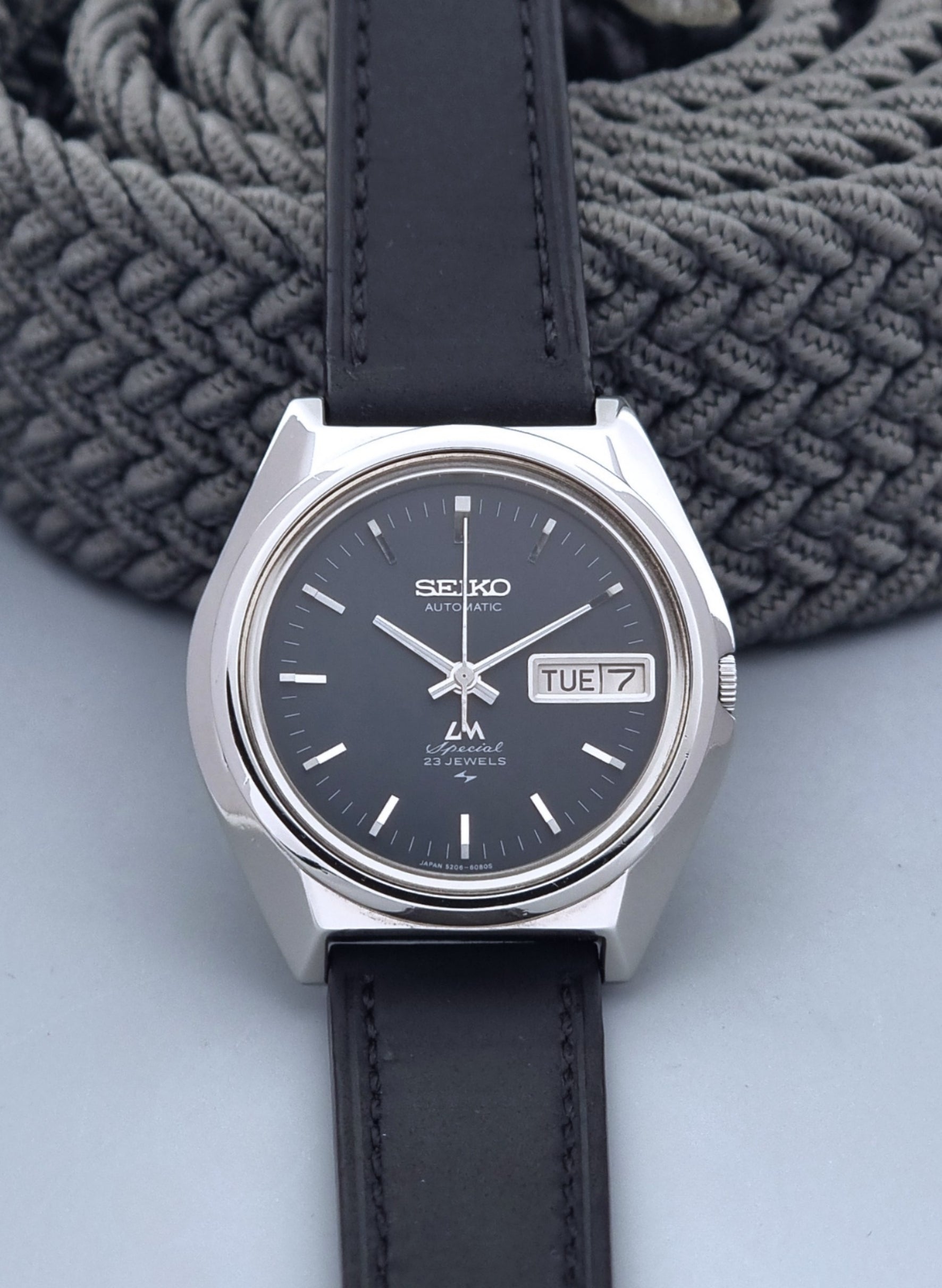 Vintage Seiko Lord Matic Special 5206-6080 watch with black leather strap on a gray background front view