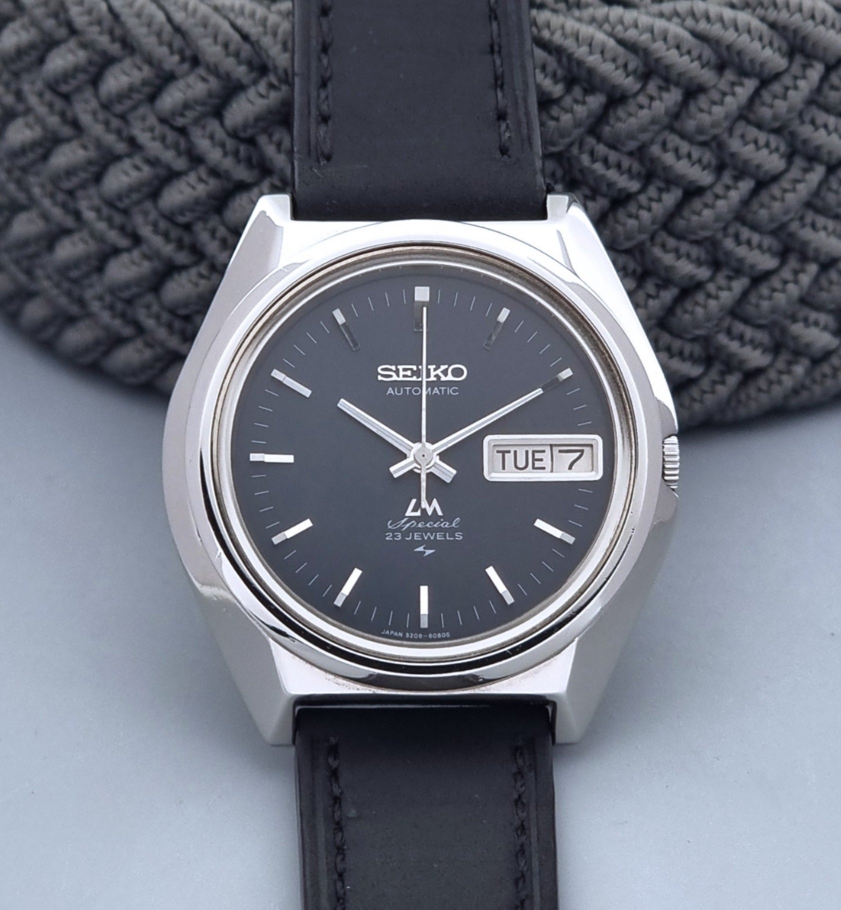 Vintage Seiko Lord Matic Special 5206-6080 watch with black leather strap on a gray background close up dial