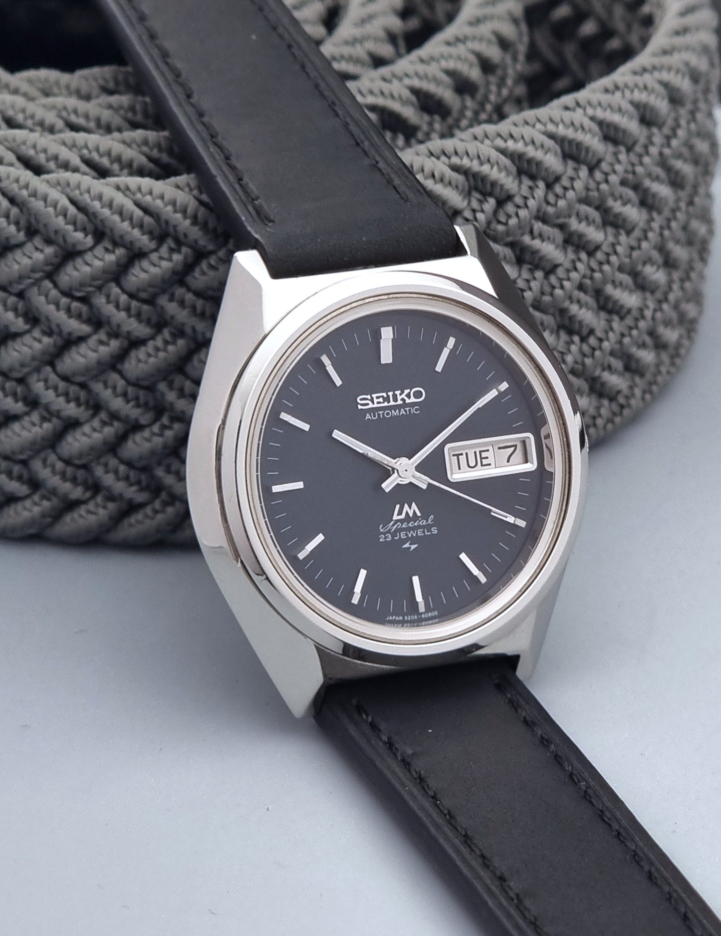 Vintage Seiko Lord Matic Special 5206-6080 watch with black leather strap on a gray background side view