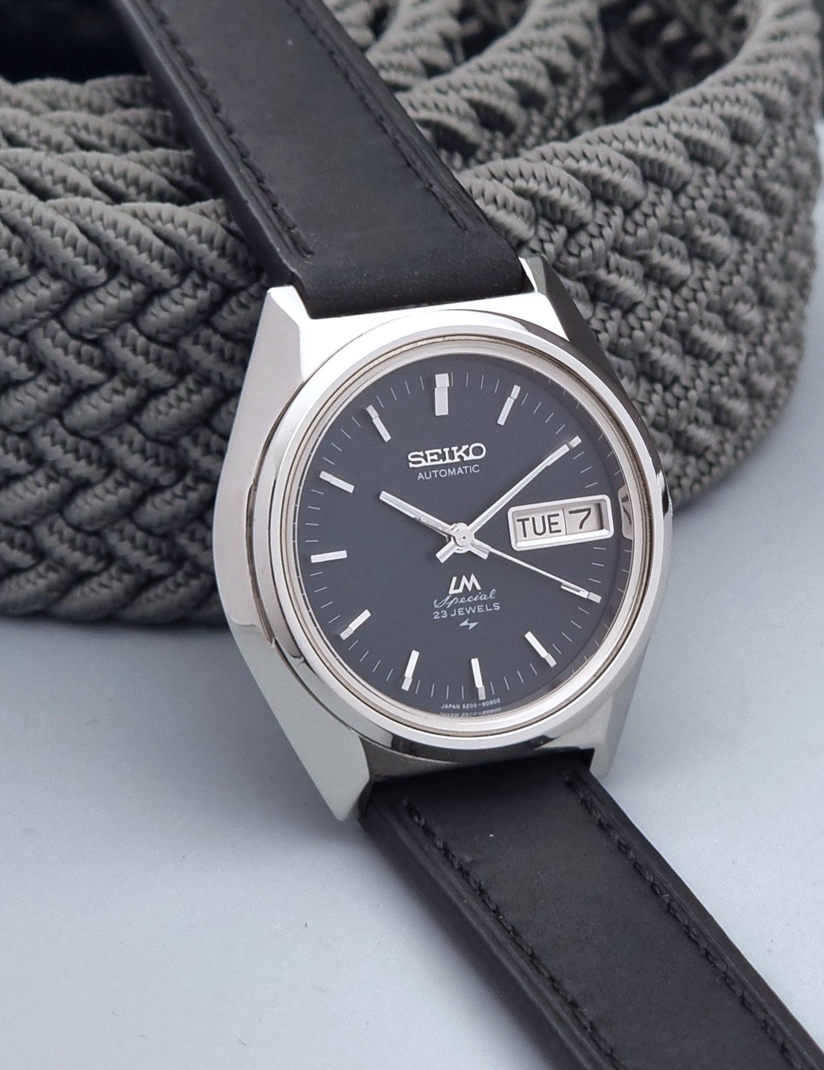Vintage Seiko Lord Matic Special 5206-6080 watch with black leather strap on a gray background side view