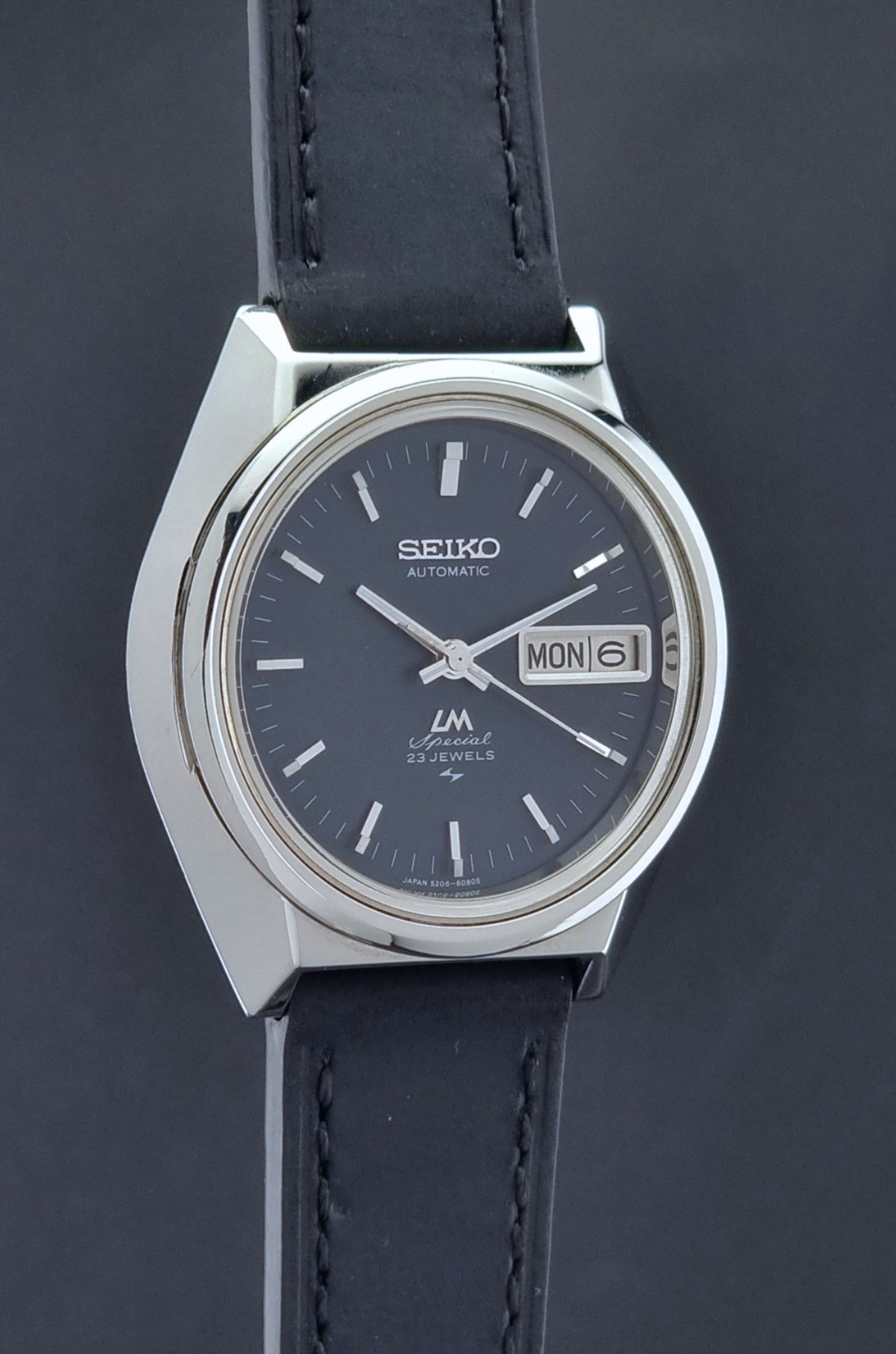 Vintage Seiko Lord Matic Special 5206-6080 watch with black leather strap on a gray background side profile