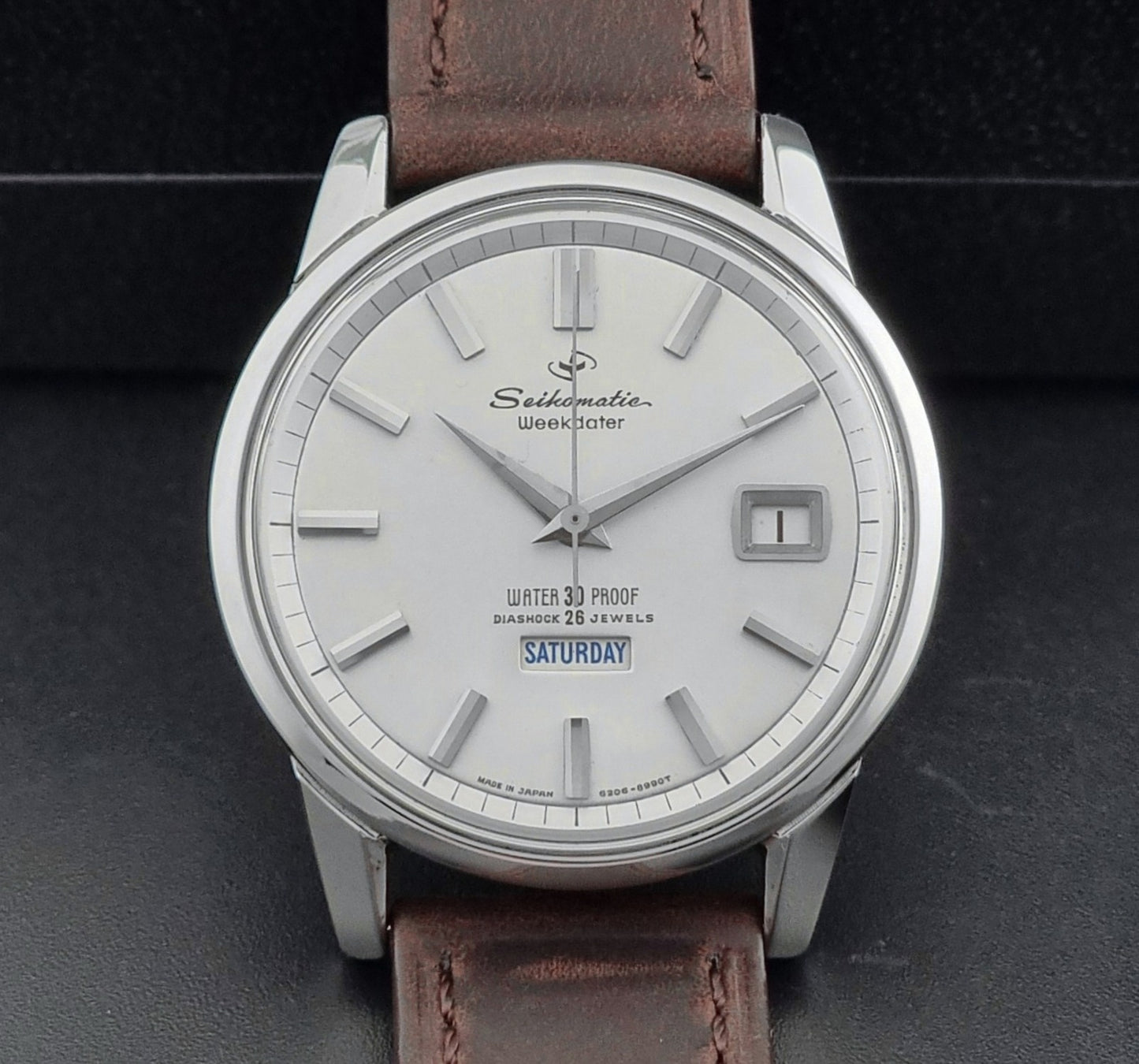 Vintage Seiko watch Seikomatic Weekdater 6206-8990 with brown leather strap on a gray textured background close up dial view