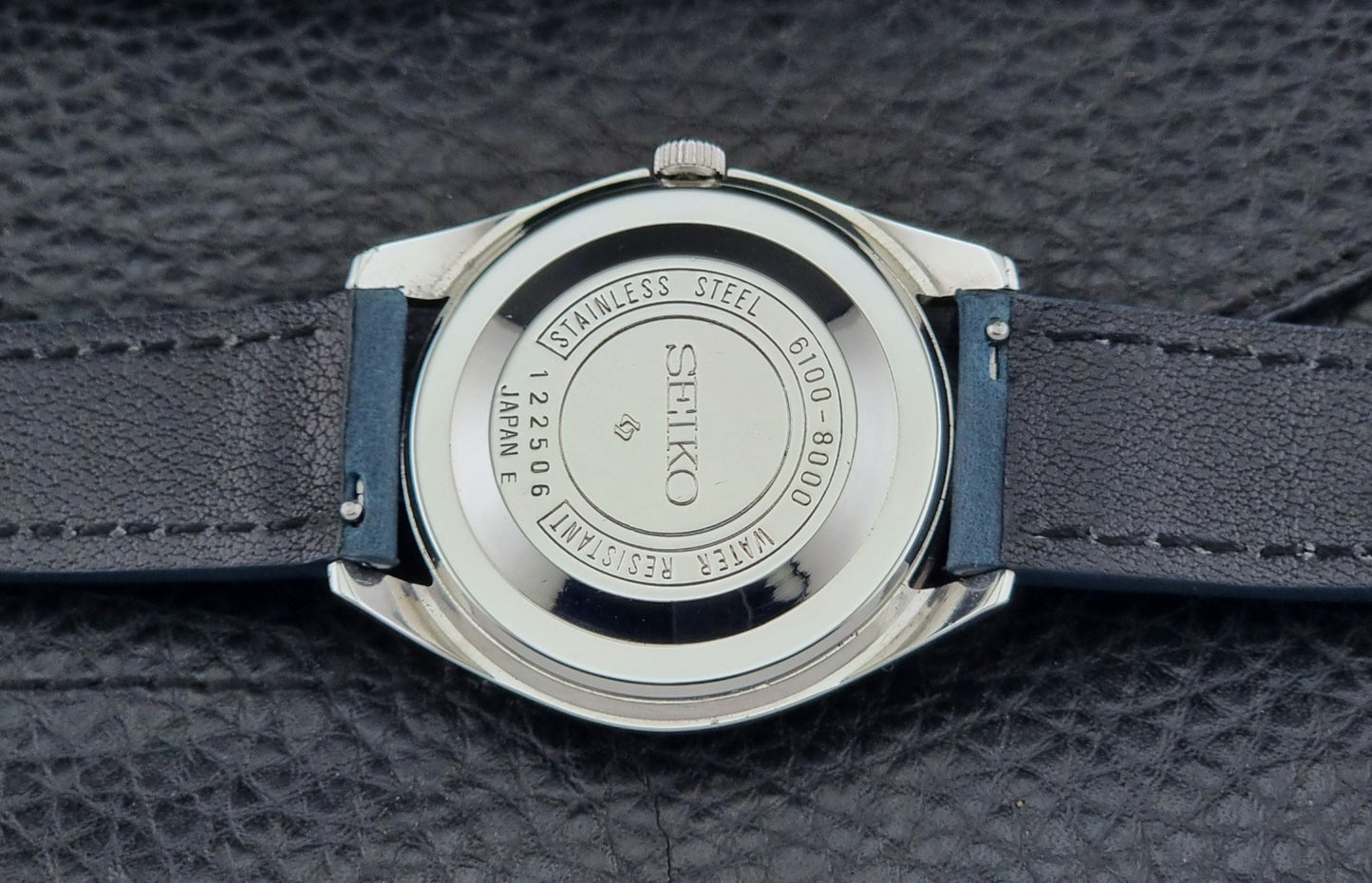 Seiko Skyliner 6100-8000 watch back with blue strap on a textured black background