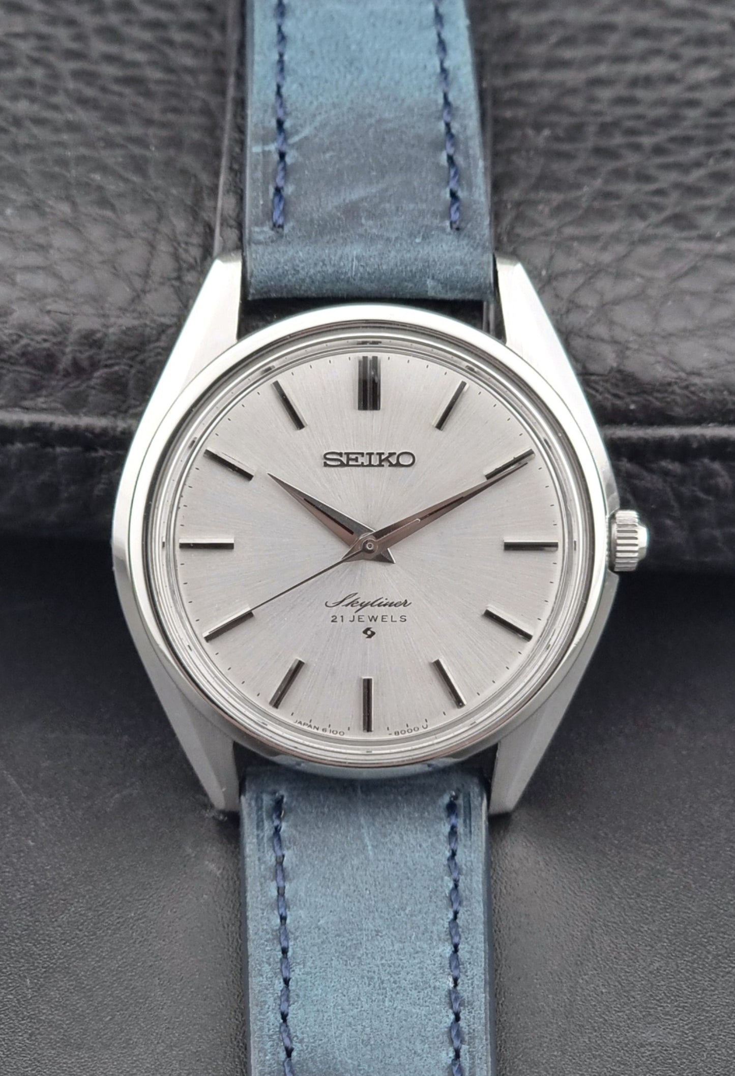 Seiko Skyliner 6100-8000 watch with a silver case and light blue leather strap on a textured gray background