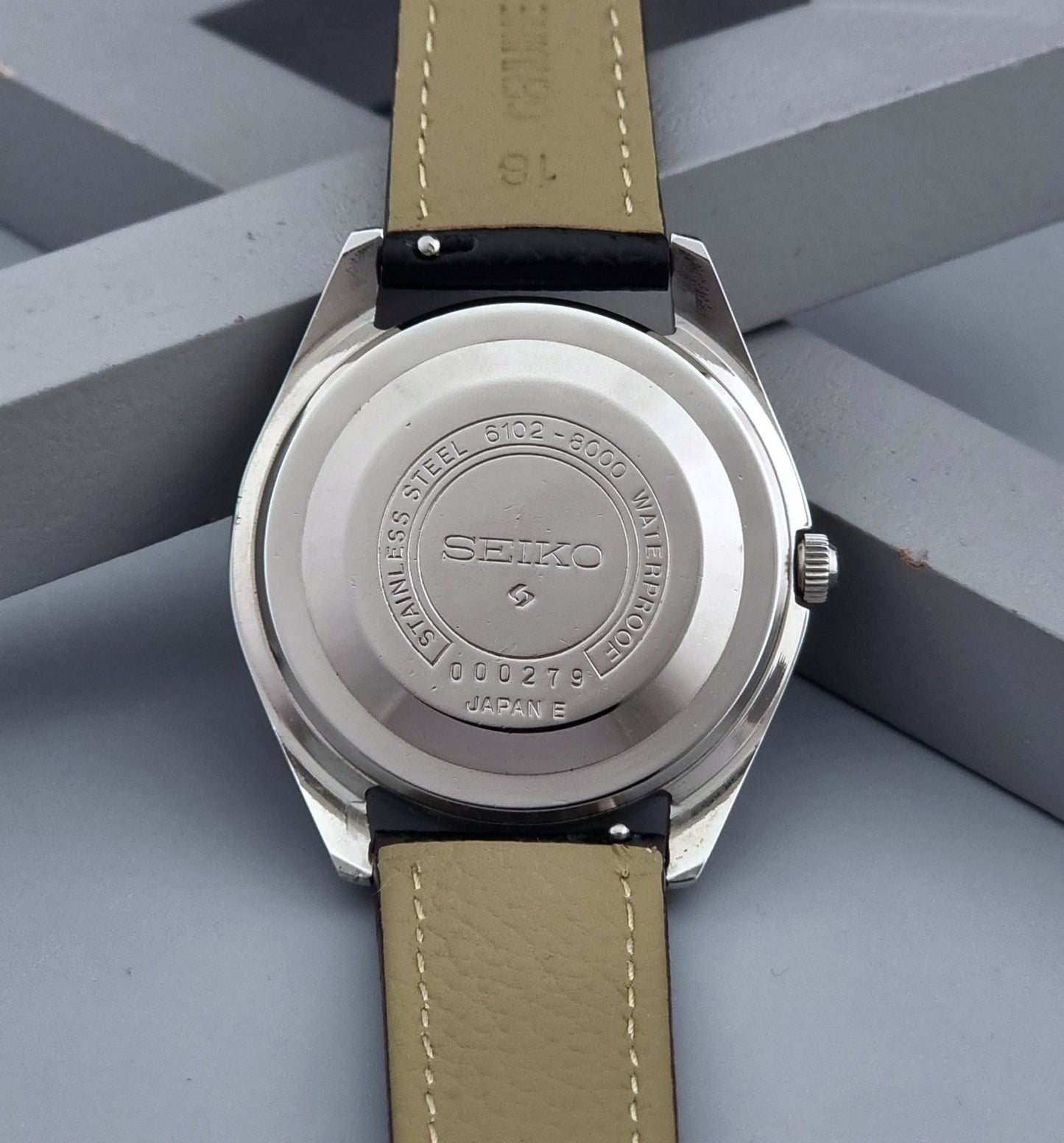 Vintage Seiko Wristwatch Skyliner 6102-8000 with black leather strap and silver case on a light gray background case back view