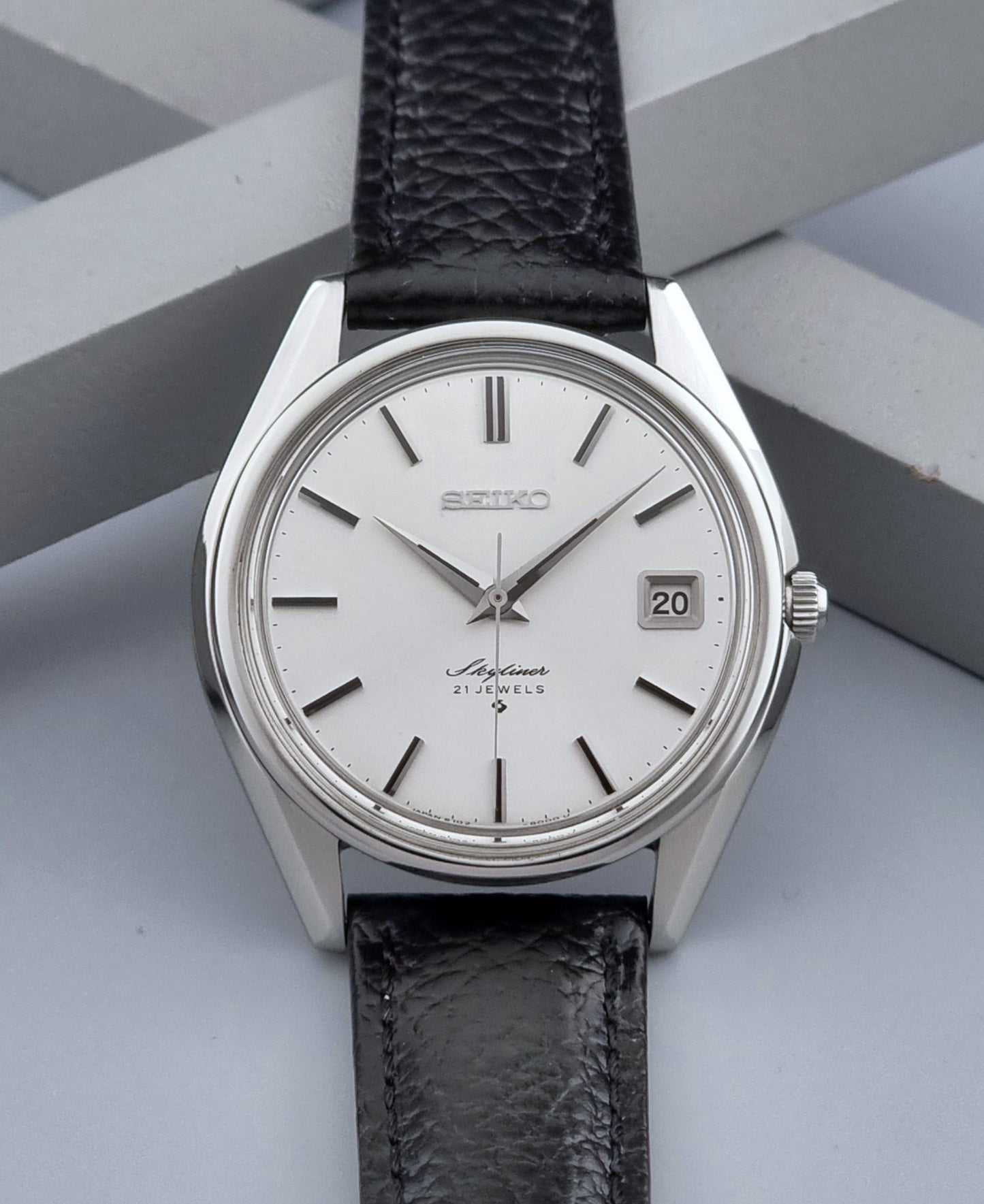 Vintage Seiko Wristwatch Skyliner 6102-8000 with black leather strap and silver case on a light gray background front view
