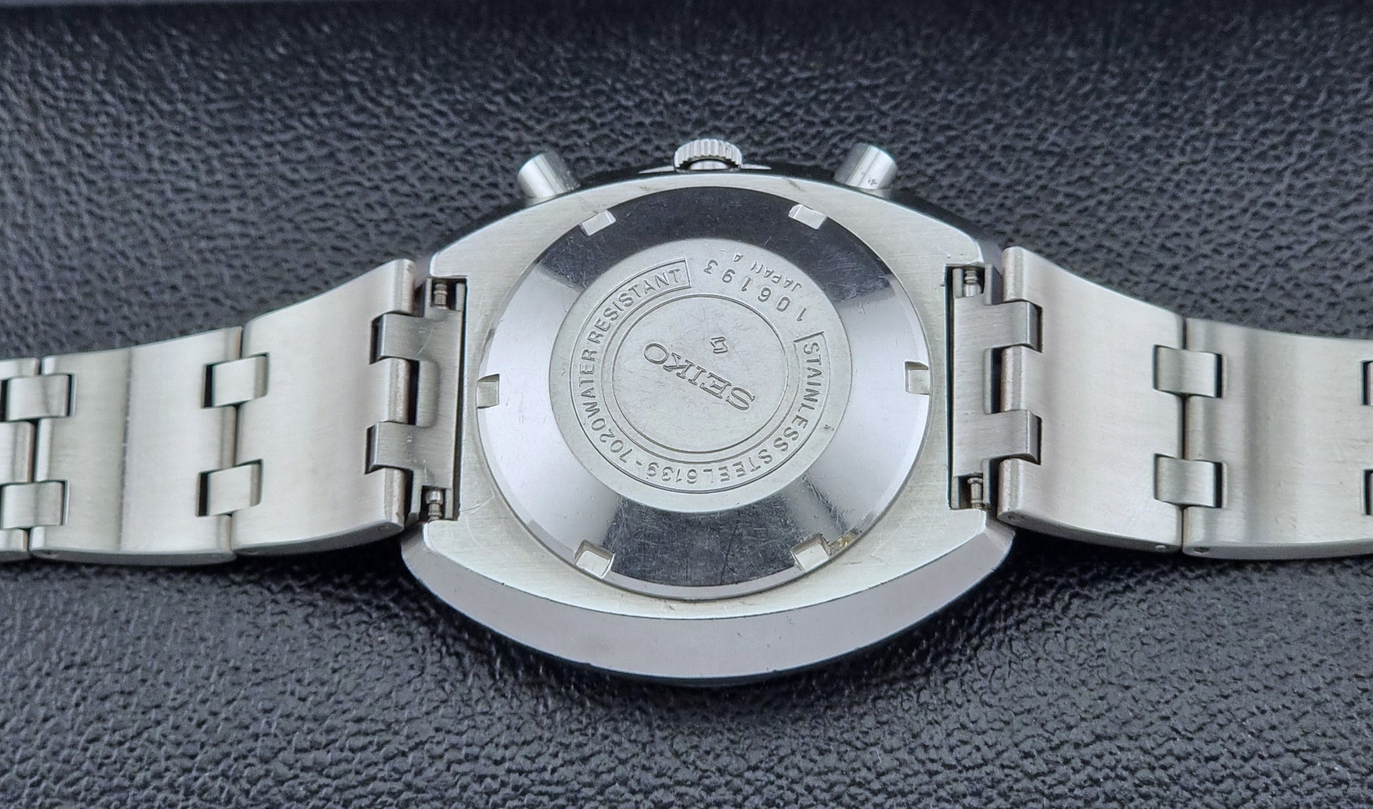 Vintage Seiko 5 sports Speedtimer 6139-7020 wristwatch with a dark face on a textured black background case back