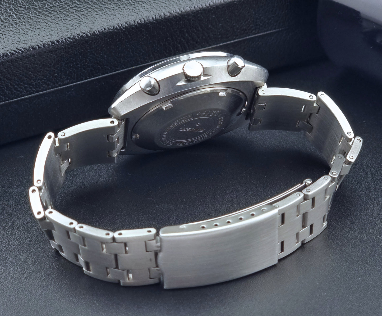 Vintage Seiko 5 sports Speedtimer 6139-7020 wristwatch with a dark face on a textured black background bracelet view