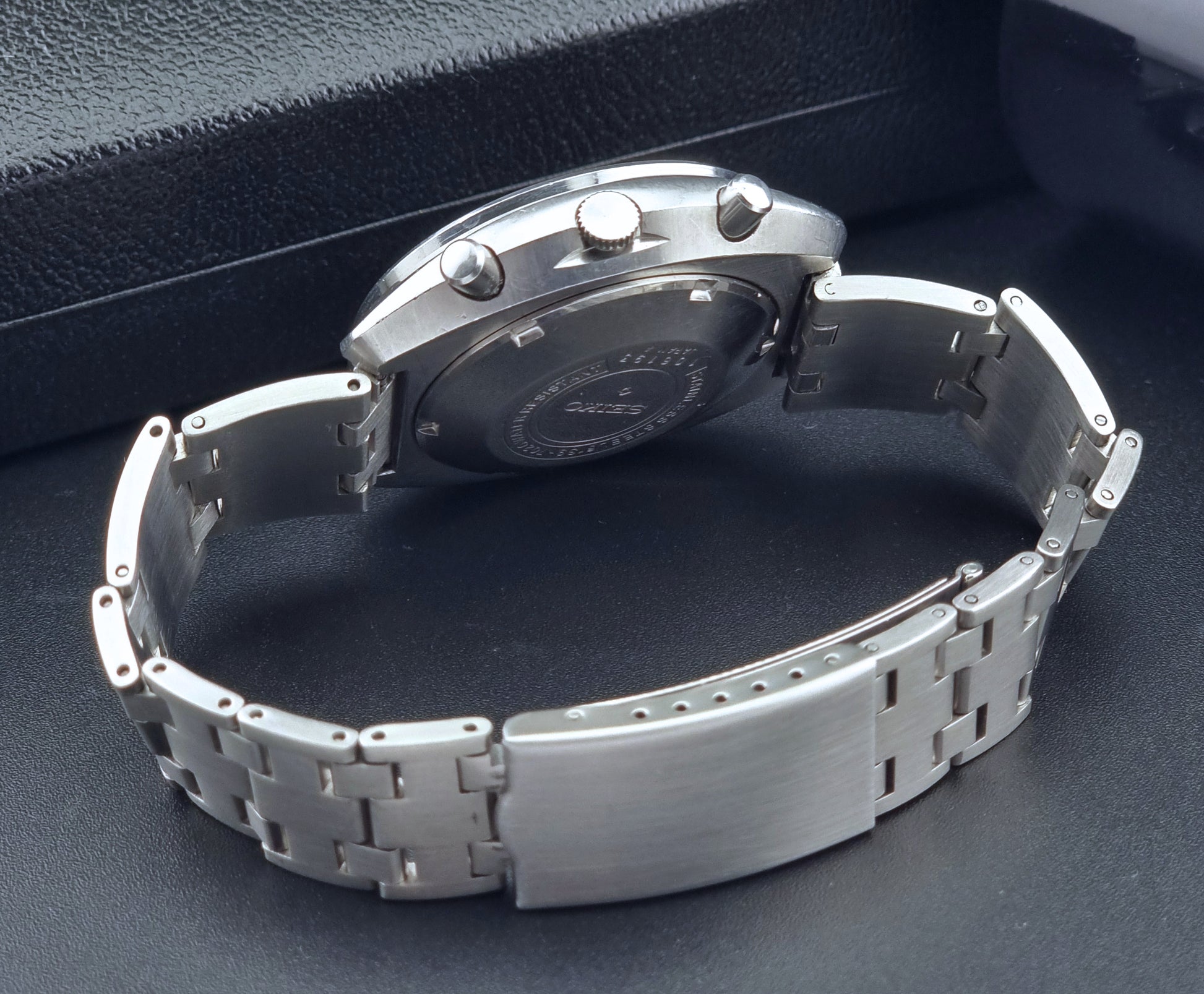 Vintage Seiko 5 sports Speedtimer 6139-7020 wristwatch with a dark face on a textured black background bracelet view