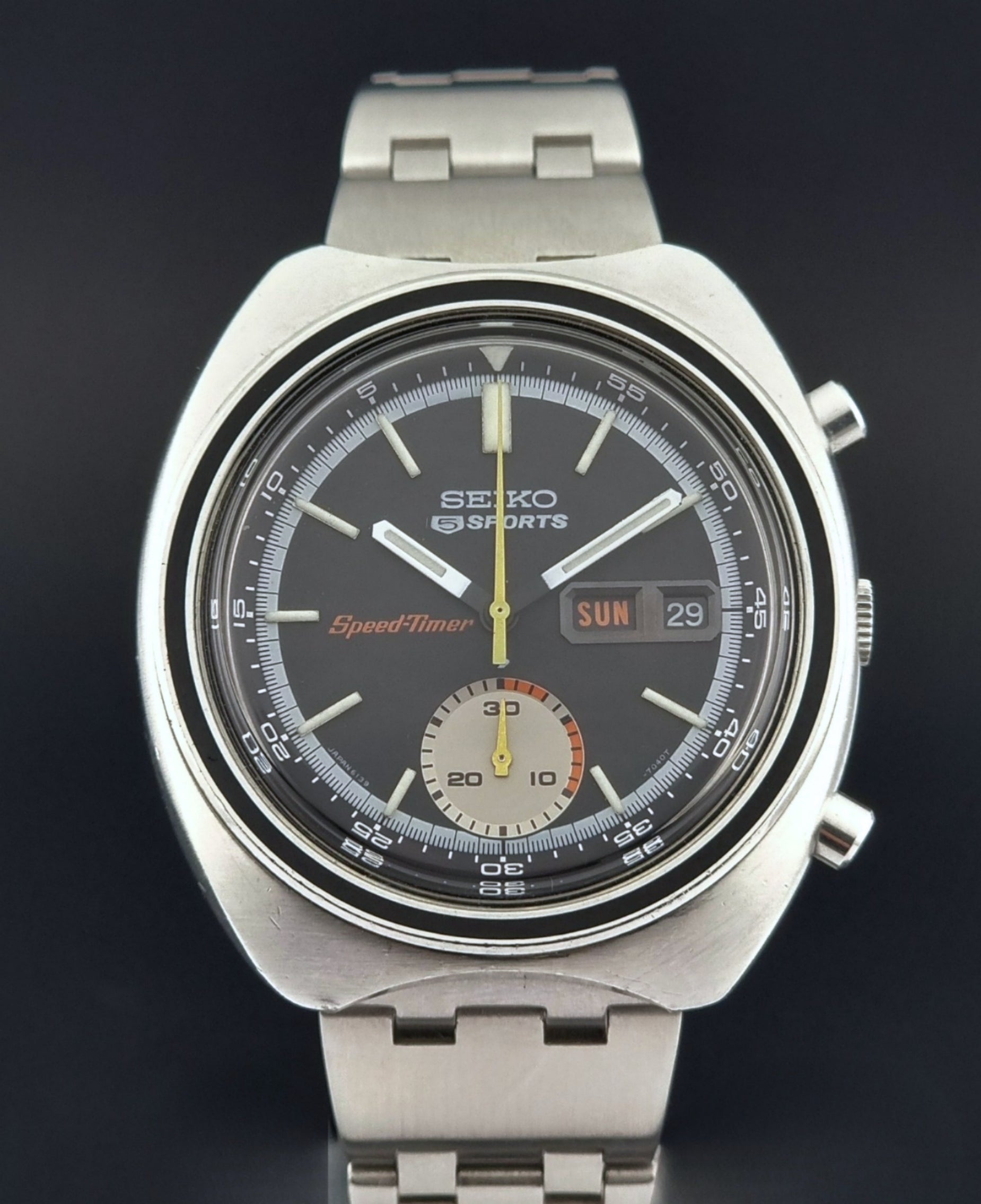 Vintage Seiko 5 sports Speedtimer 6139-7020 wristwatch with a dark face on a textured black background close up