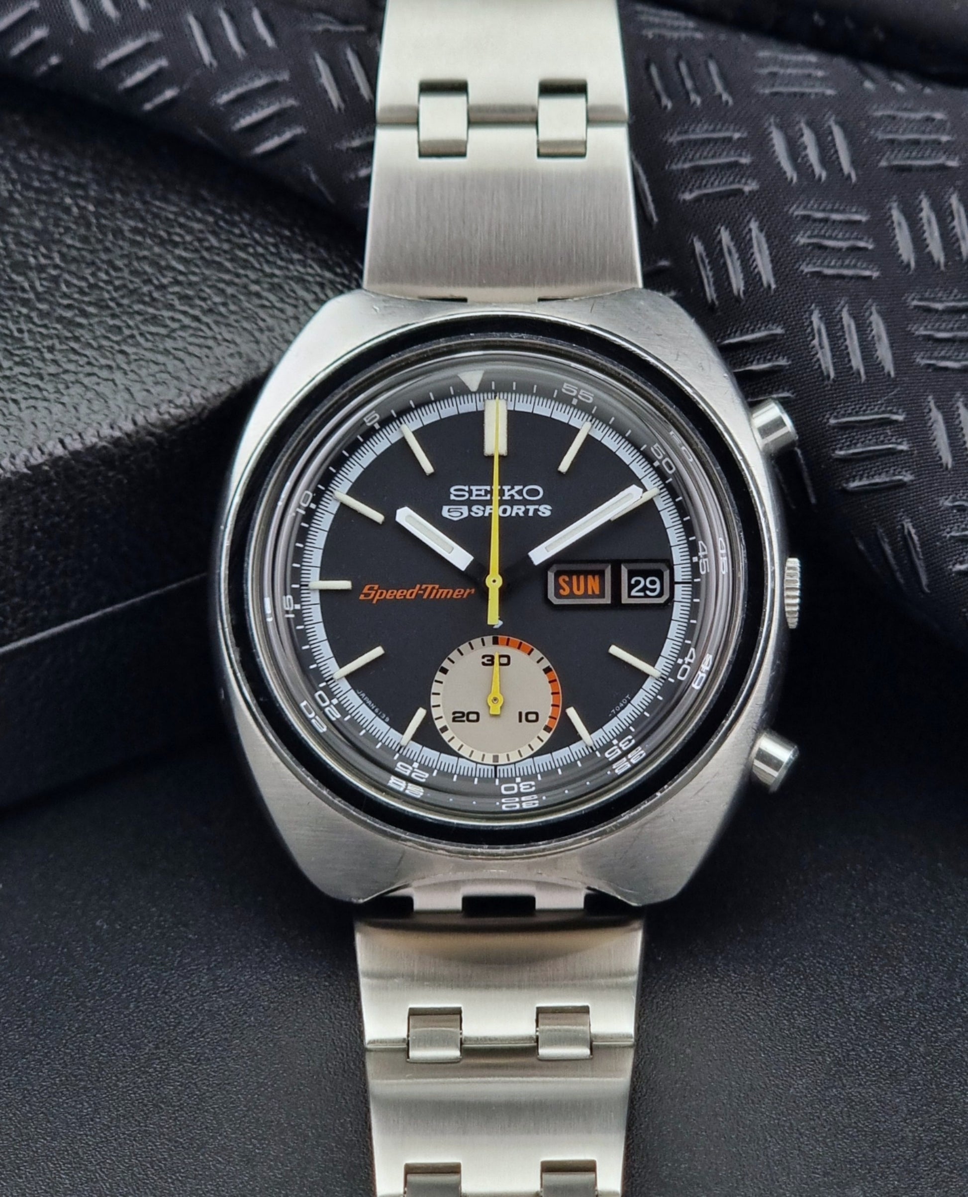 Vintage Seiko 5 sports Speedtimer 6139-7020 wristwatch with a dark face on a textured black background front view
