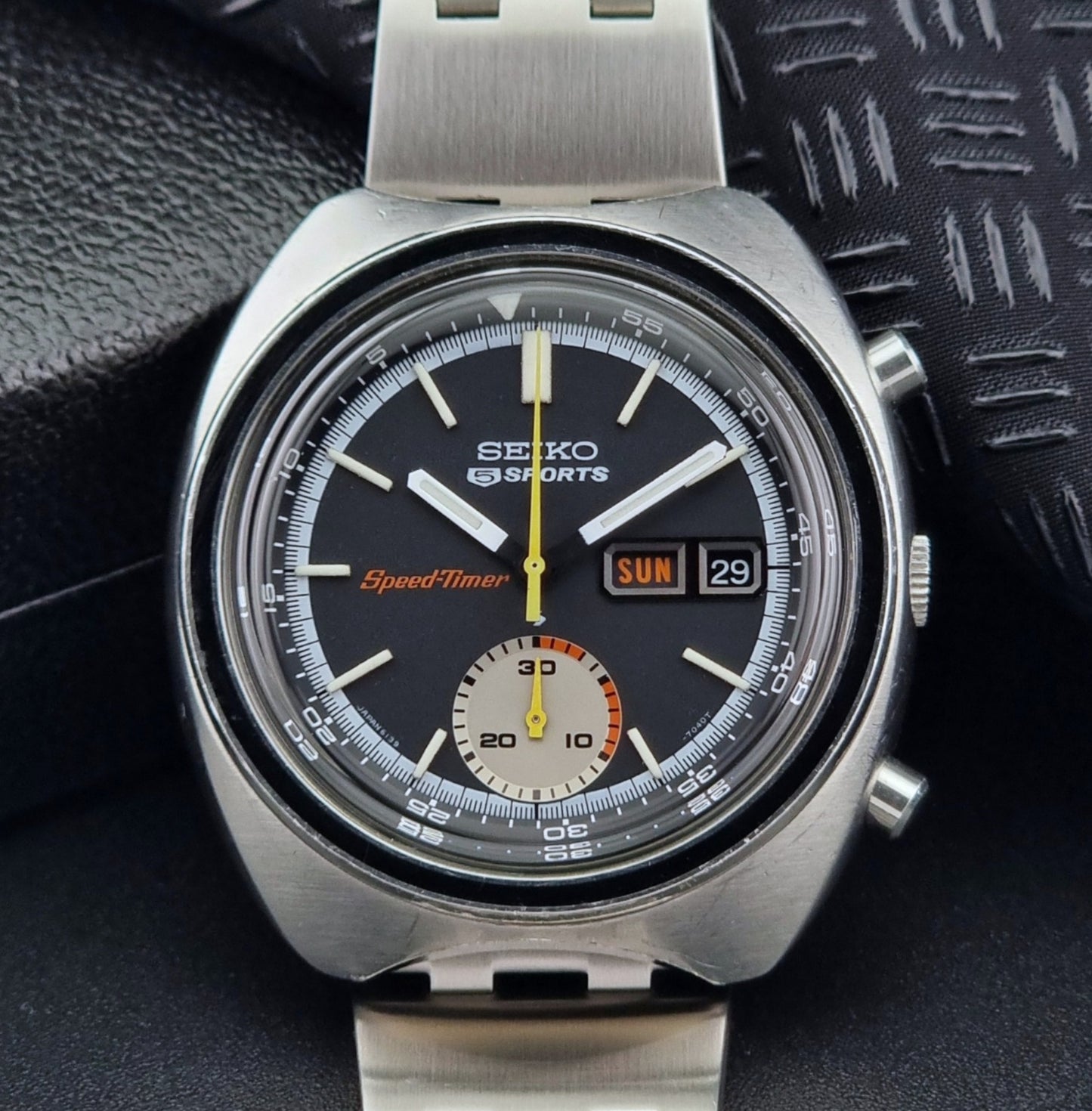 Vintage Seiko 5 sports Speedtimer 6139-7020 wristwatch with a dark face on a textured black background close up dial view