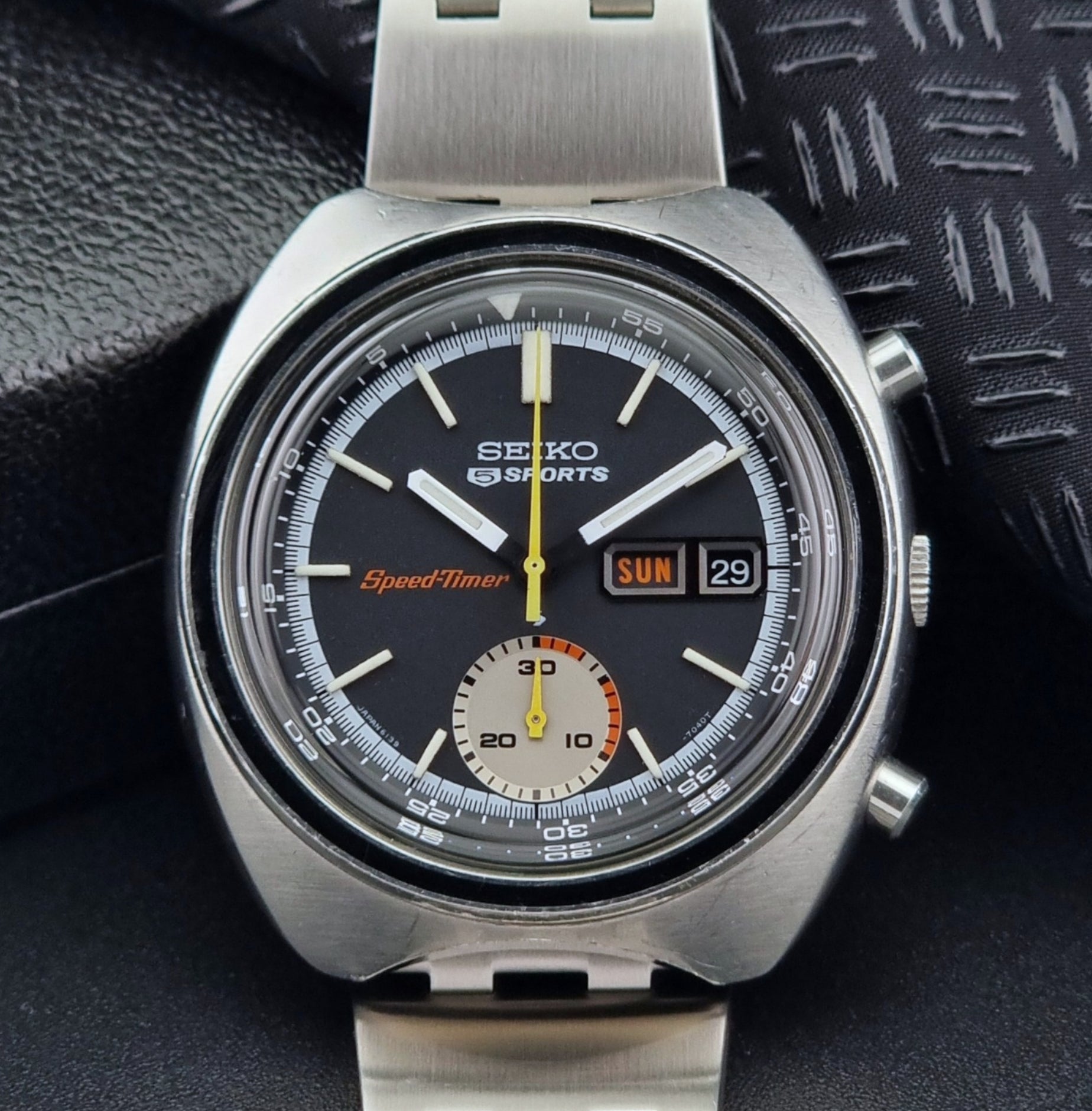 Vintage Seiko 5 sports Speedtimer 6139-7020 wristwatch with a dark face on a textured black background close up dial view