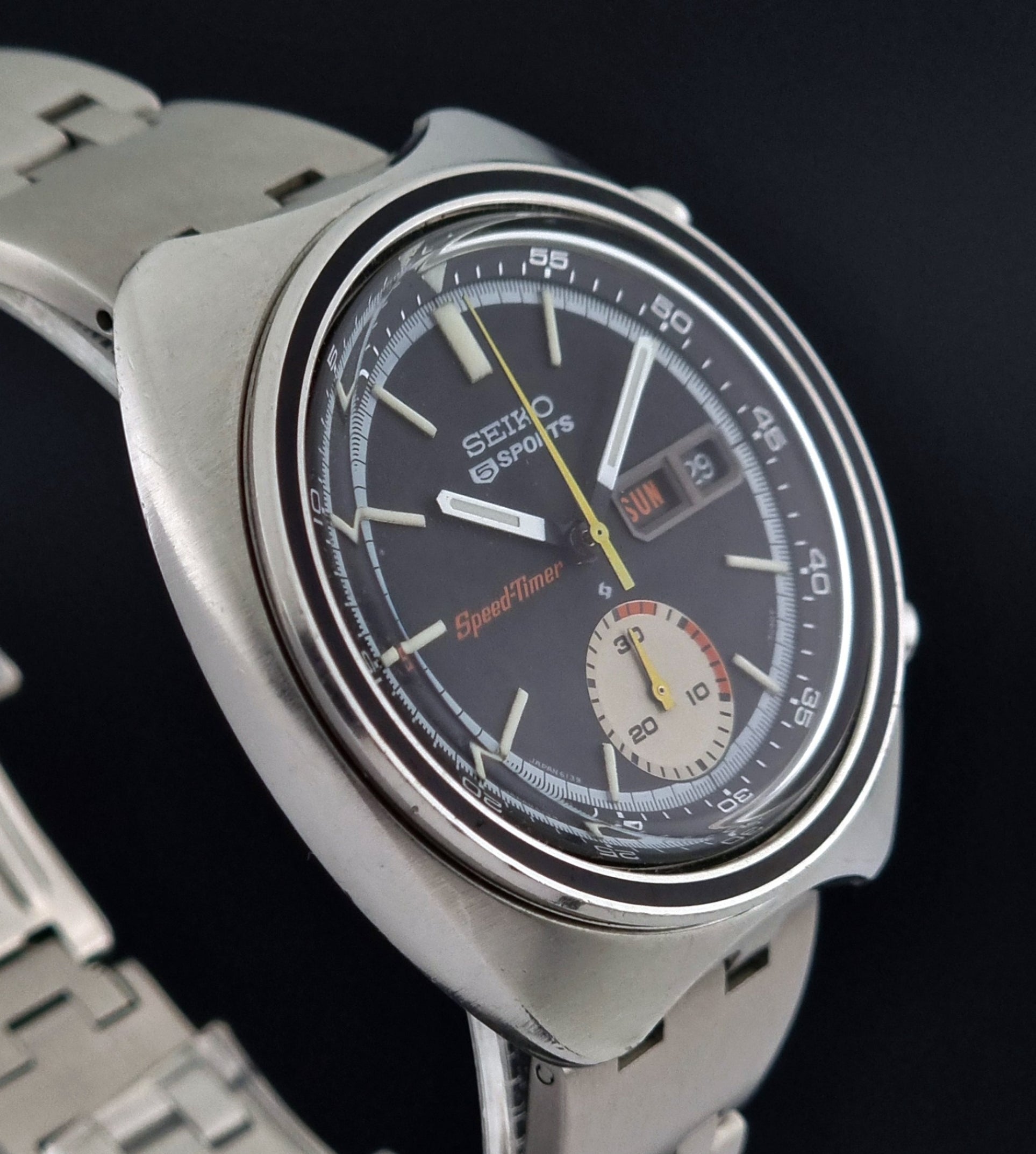 Vintage Seiko 5 sports Speedtimer 6139-7020 wristwatch with a dark face on a textured black background side profile