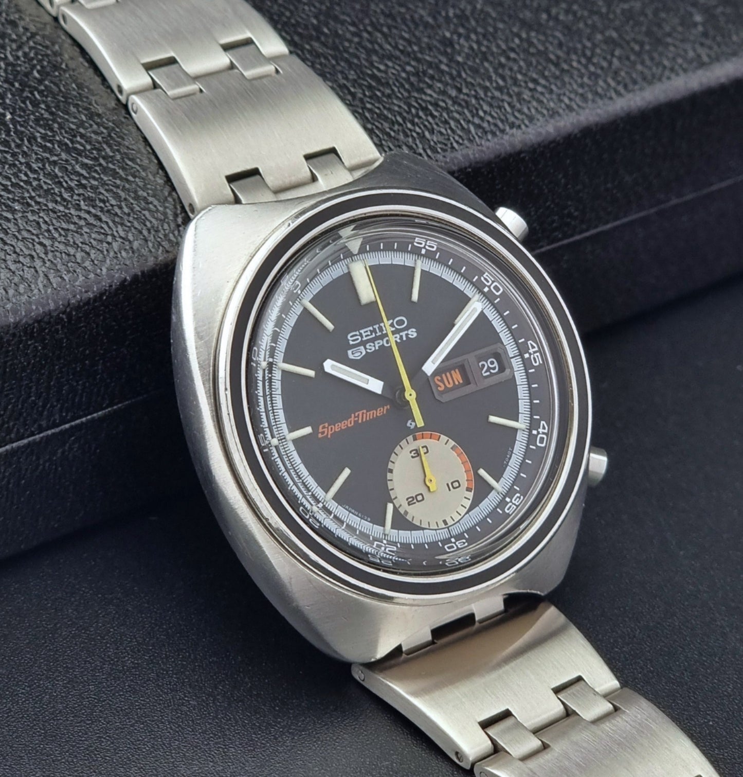 Vintage Seiko 5 sports Speedtimer 6139-7020 wristwatch with a dark face on a textured black background side view