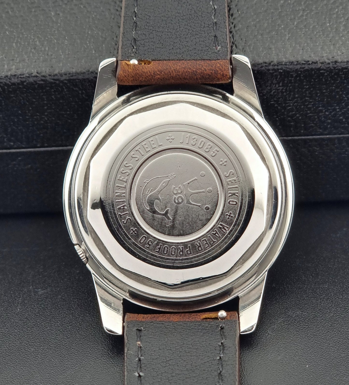 Vintage Seiko Wristwatch Seikomatic J13085 brown leather strap on a dark textured surface case back view