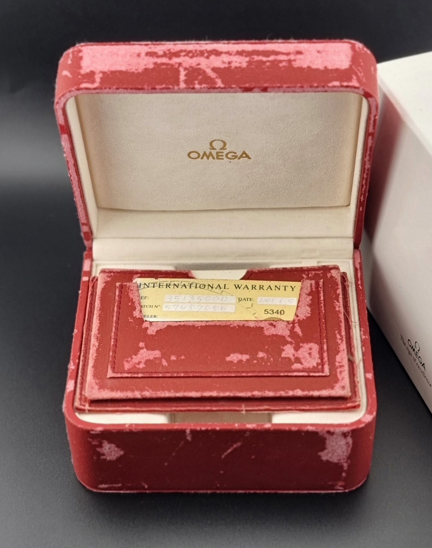 Red Omega watch box with an International Warranty card on a dark background