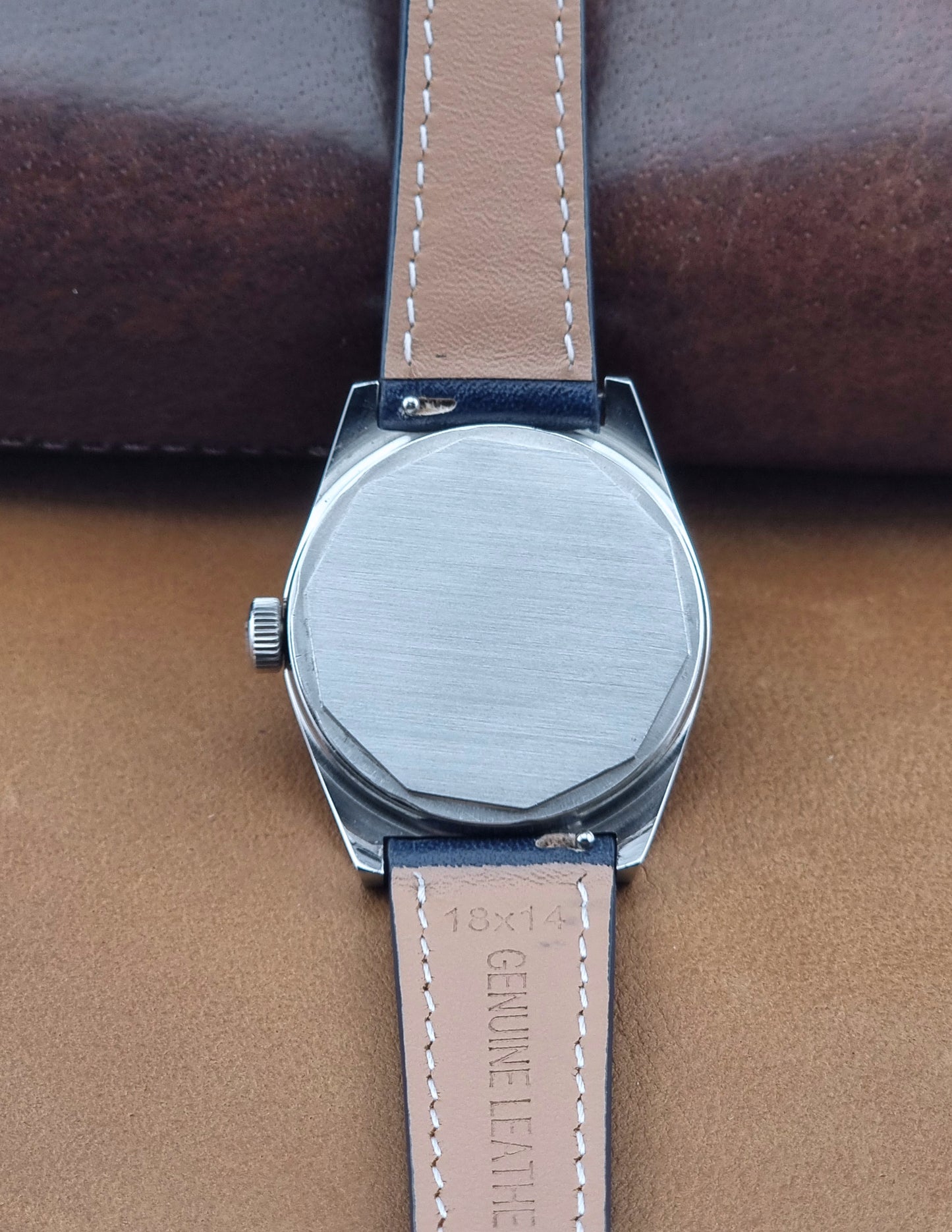 Close-up Vintage Tissot Wristwatch 41620 PR 516 of the back of a wristwatch with a brushed metal case and a tan leather strap on a brown leather surface.