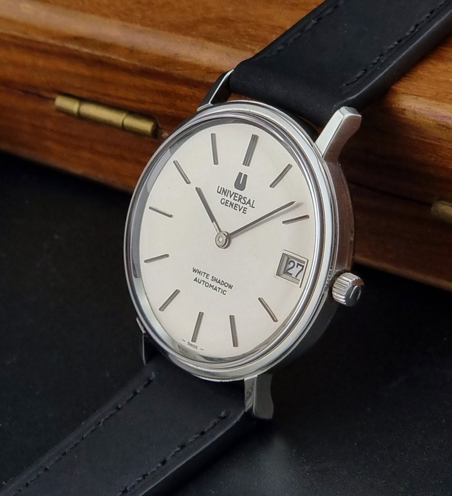 Universal Geneve Watch with black strap and white dial on a wooden surface