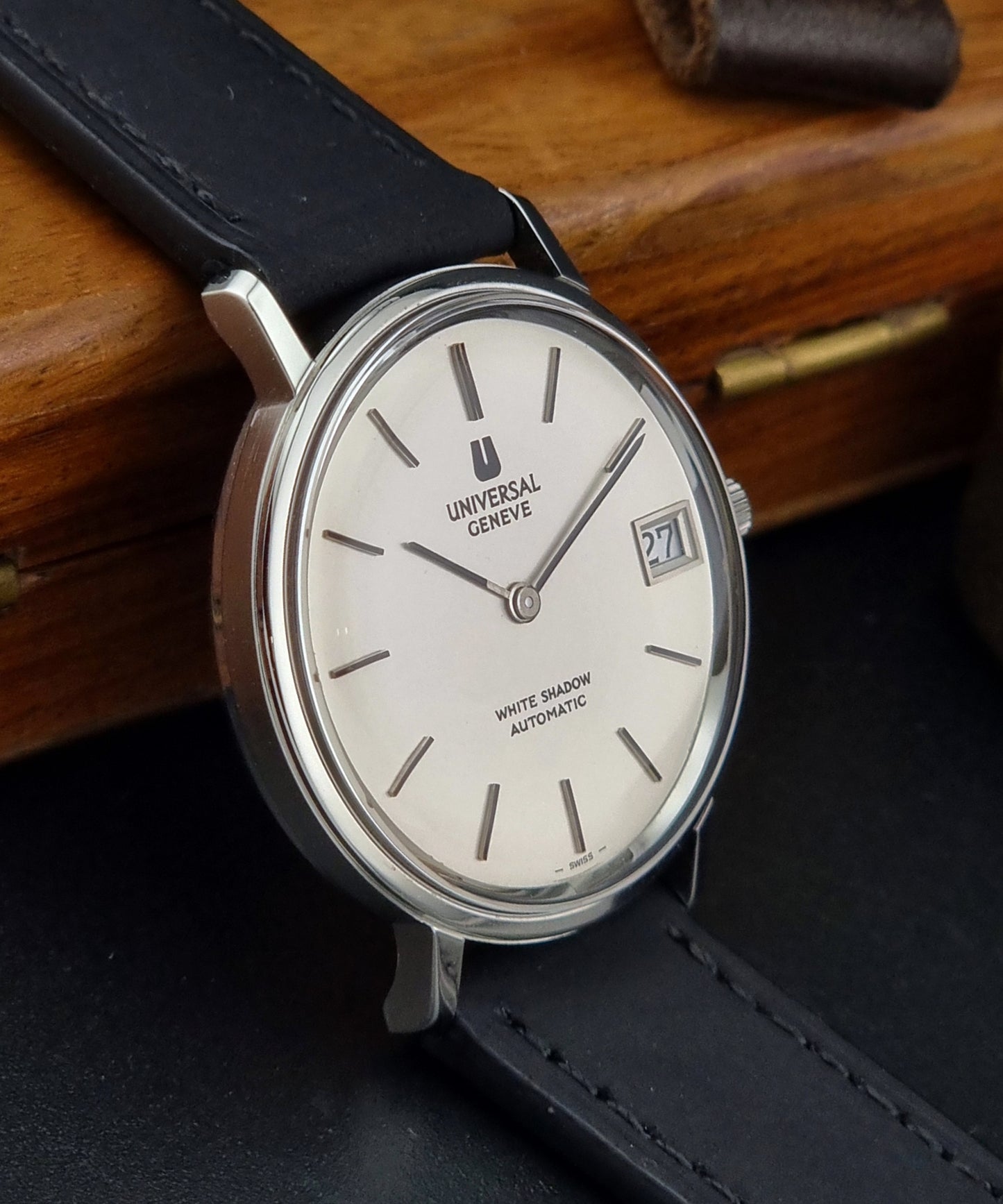 Universal Geneve Watch with black leather strap and white face on a wooden surface