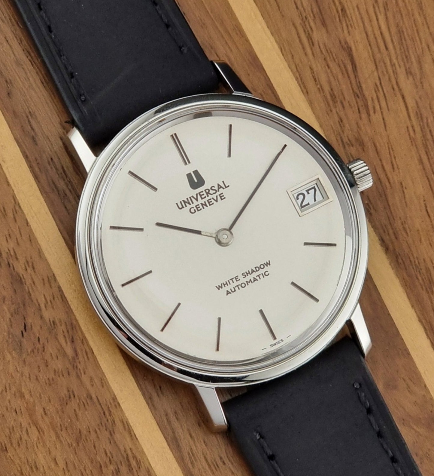 Universal Geneve Watch with black strap and white face on a wooden surface