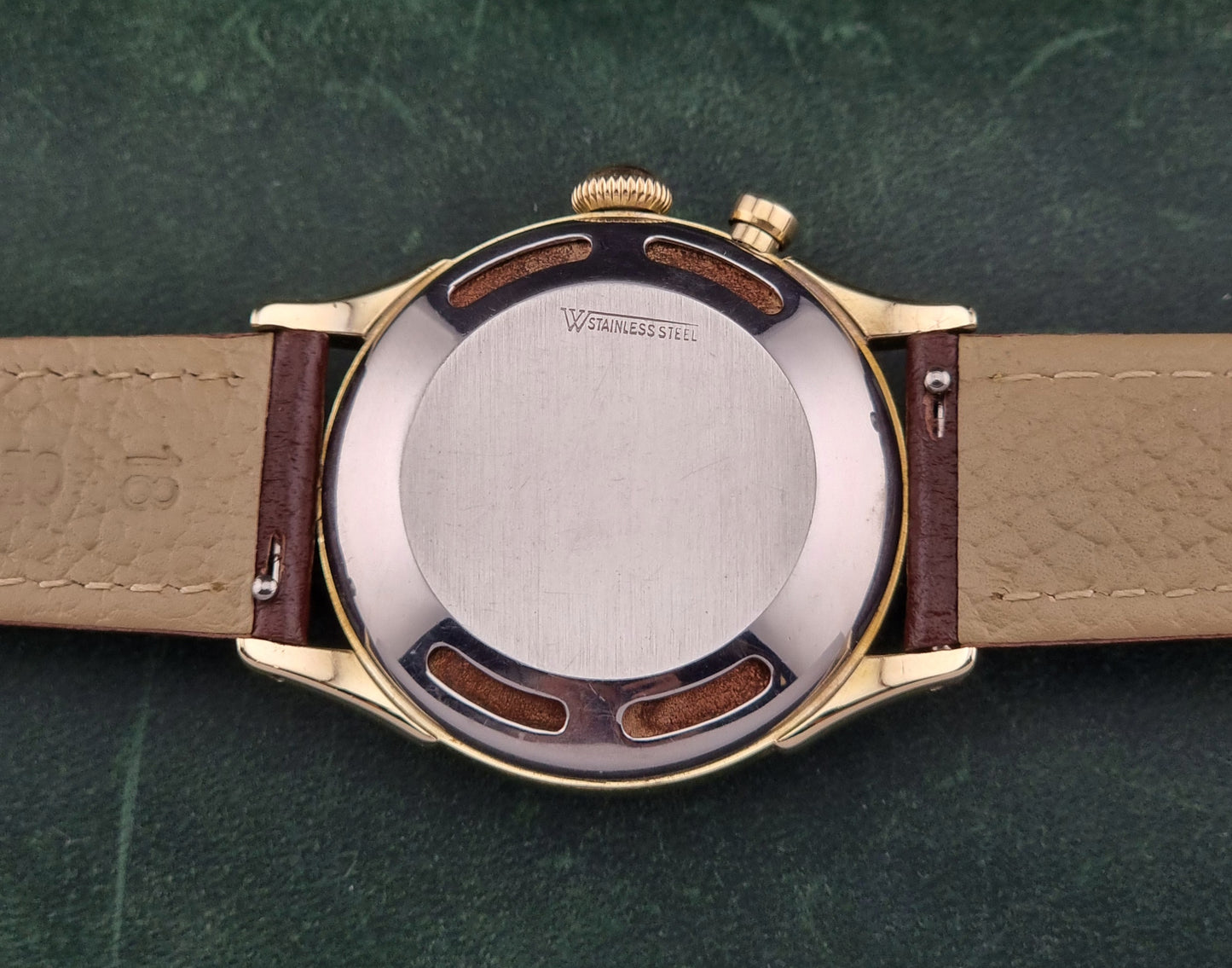 Vulcain cricket W197446 Close-up of a watch back cover with 'Stainless Steel' engraving on a green textured background