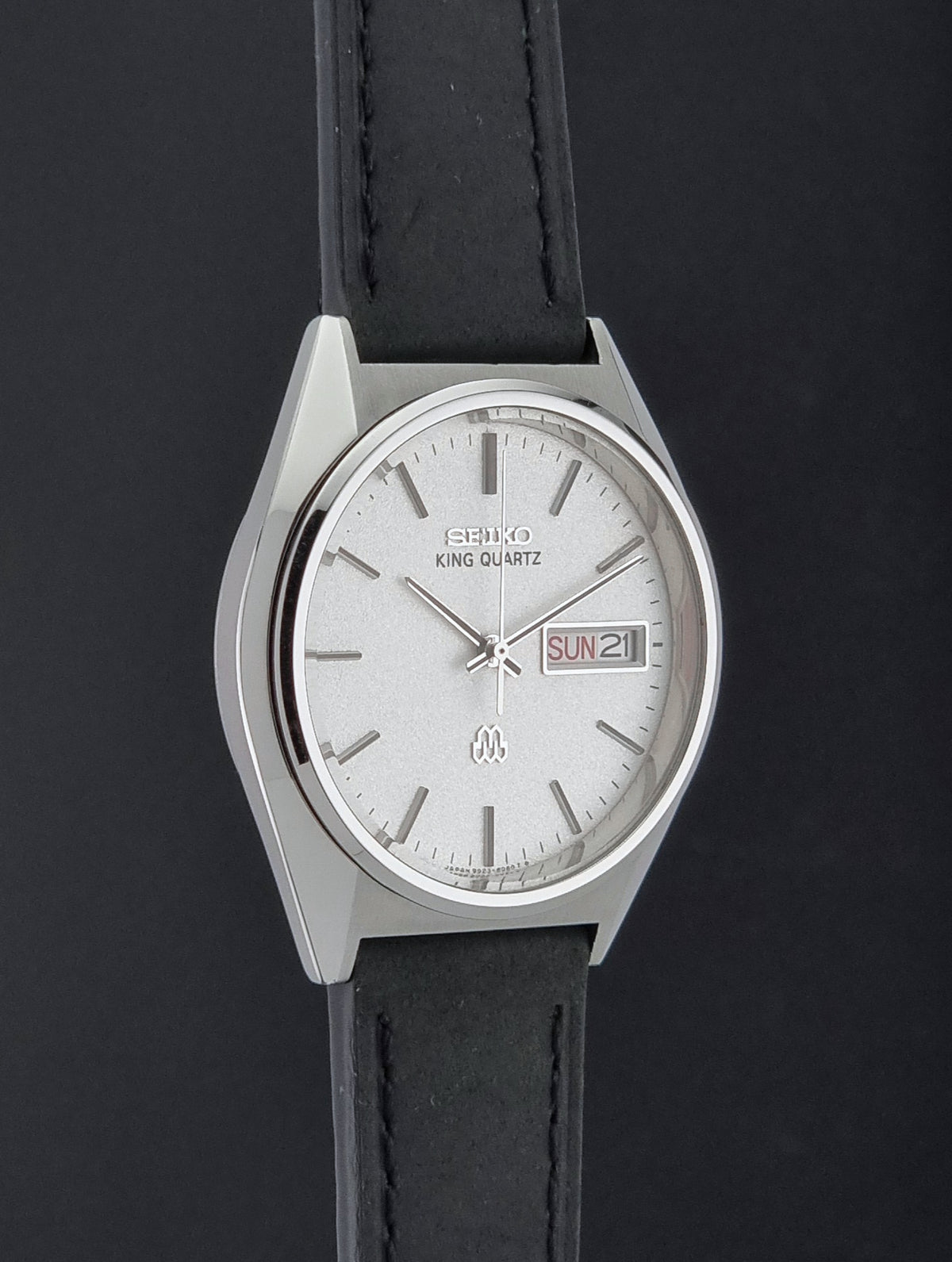 A vintage Seiko King Quartz wristwatch with a silver-tone metal case, white dial, and black leather strap, shown against a dark background.