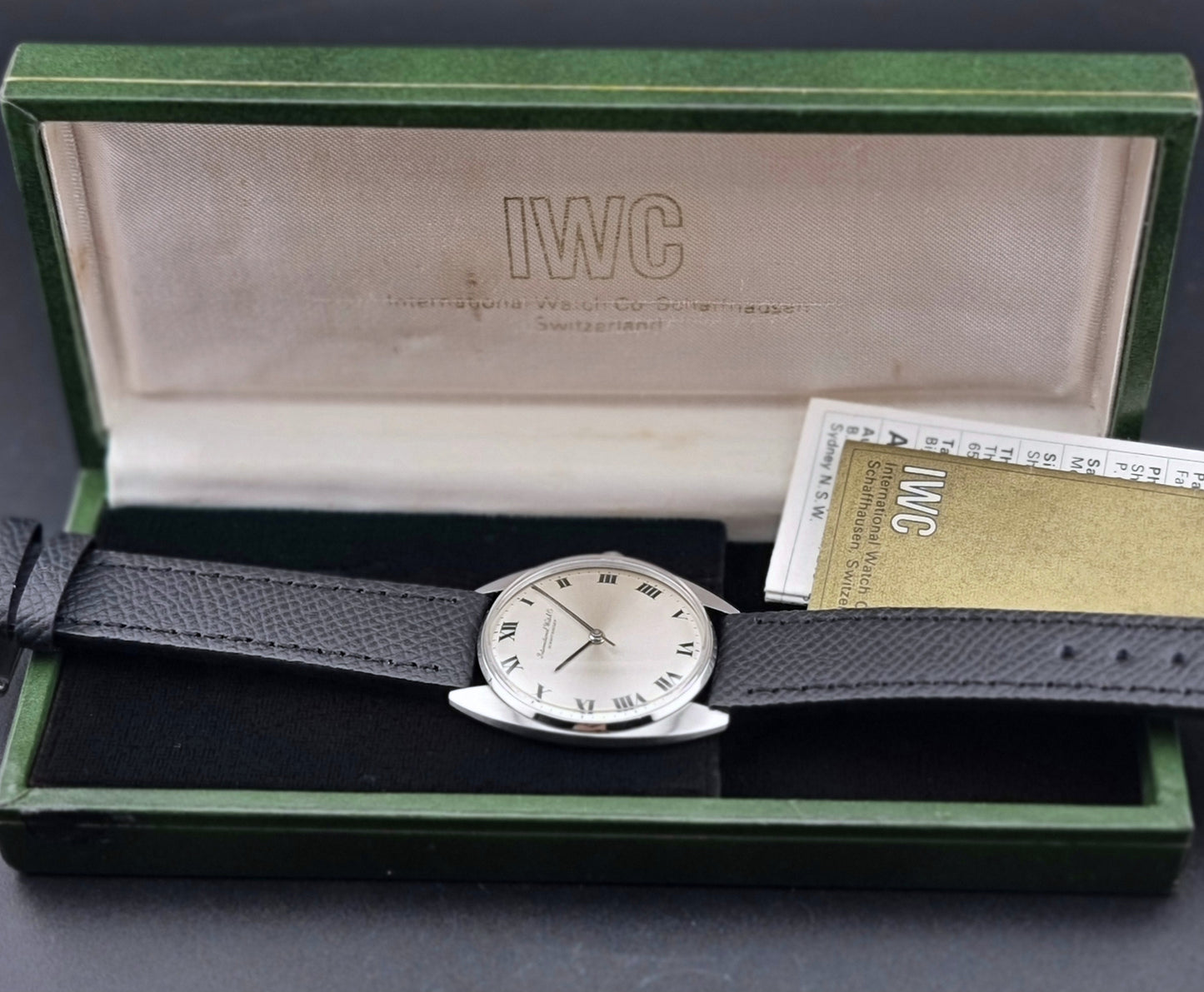 Vintage IWC R1419 Wristwatch with a black strap and silver dial on a dark background box view