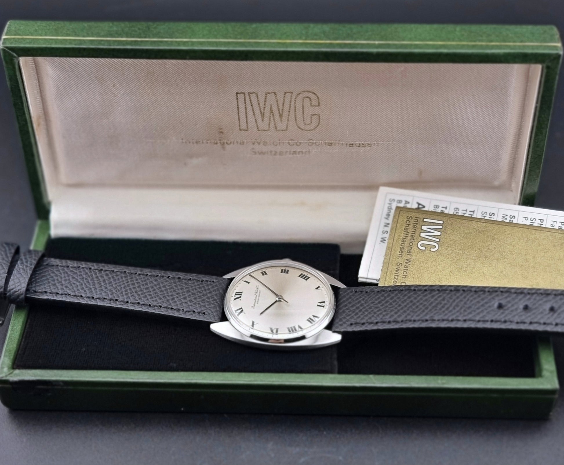 Vintage IWC R1419 Wristwatch with a black strap and silver dial on a dark background box view
