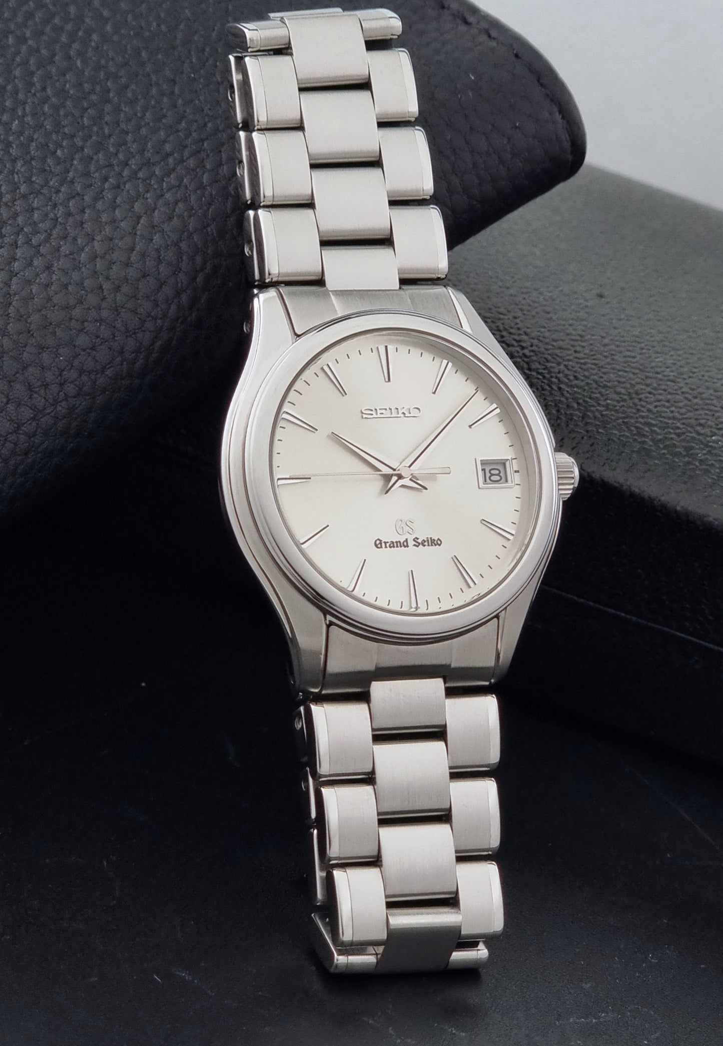 A Grand Seiko SBGX005 quartz watch 9F62-0A10 Sunburst Dial  with bracelet on a dark back ground resting n a textured background