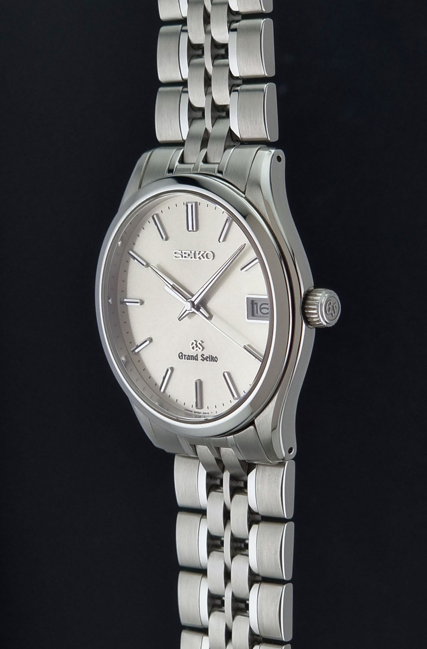 A Grand Seiko SBGV001 quartz watch and link bracelet and a cream-colored dial, shown against a solid black back background