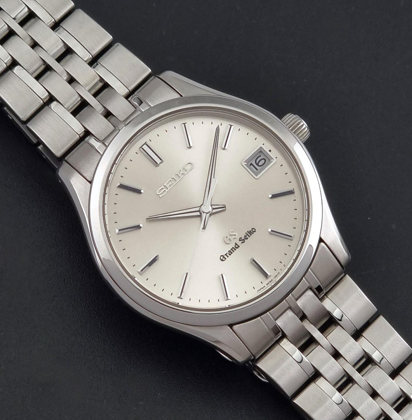 A Grand Seiko SBGV001 quartz watch and link bracelet and a cream-colored dial, with silver-tone hour markers and a date window.