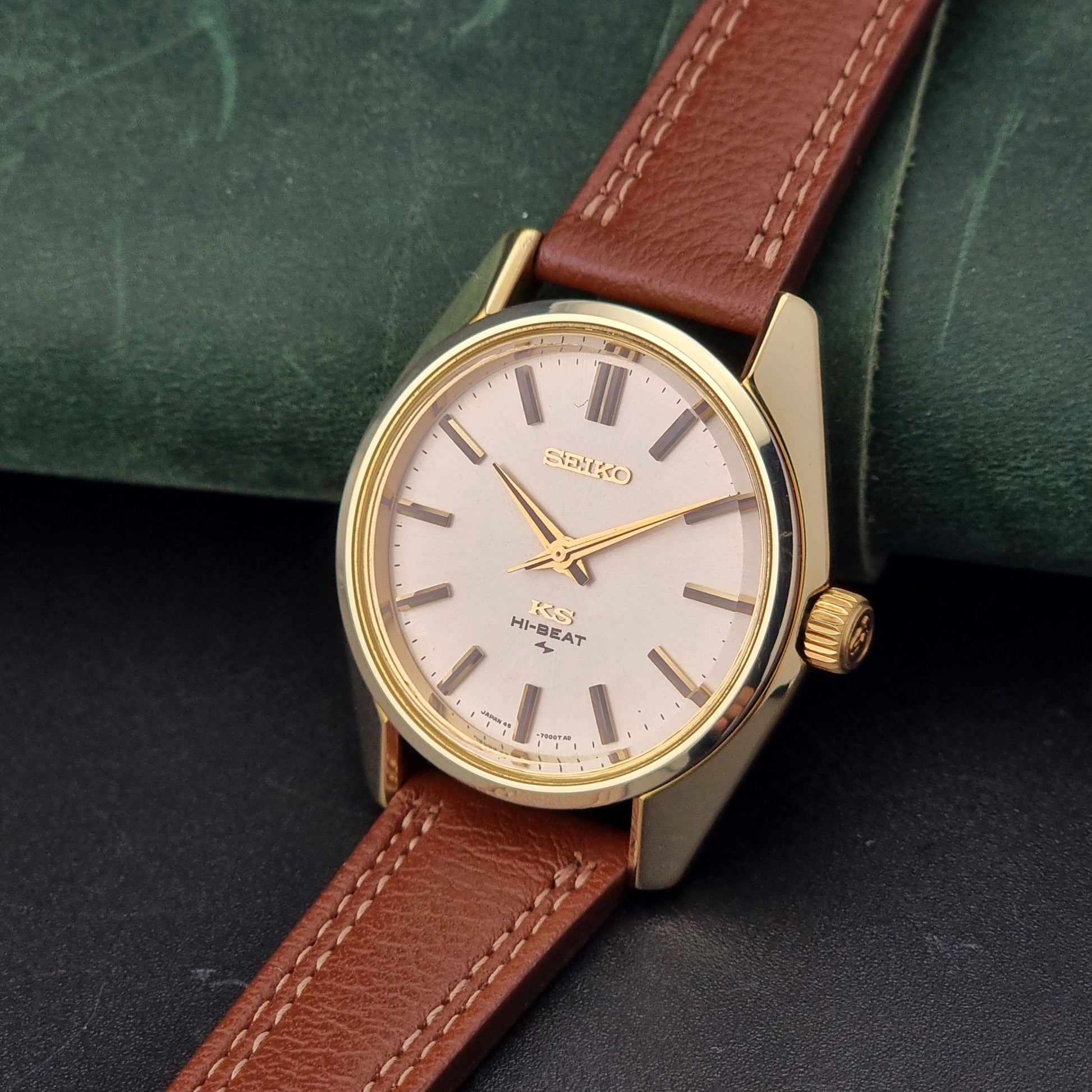 Vintage King Seiko watch with brown leather strap and gold casing on a dark surface.