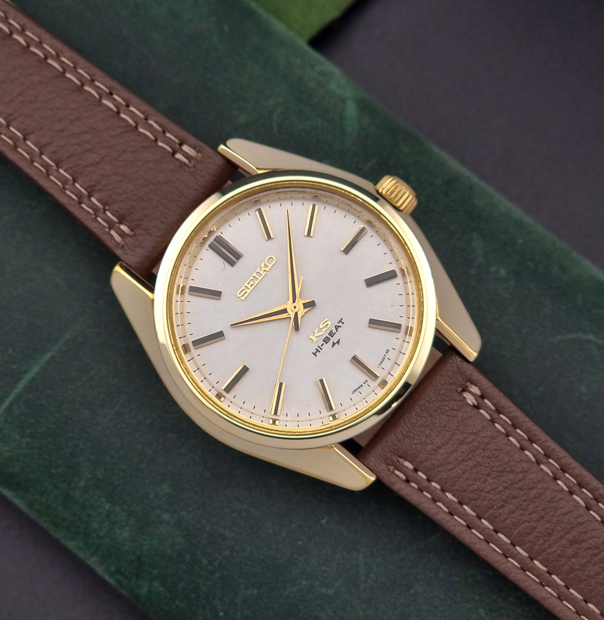 Vintage King Seiko watch with gold case and brown leather strap on a green surface