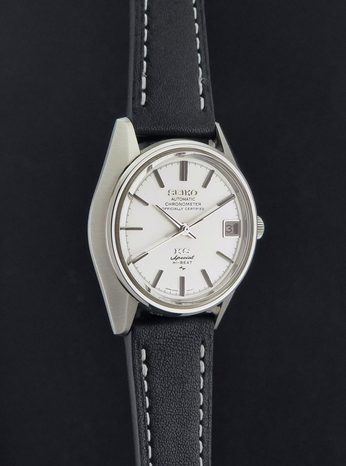 A Vintage King Seiko Special 5245-6010 Watch, white dial, and black leather strap with white stitching, photographed side profile against a dark background.