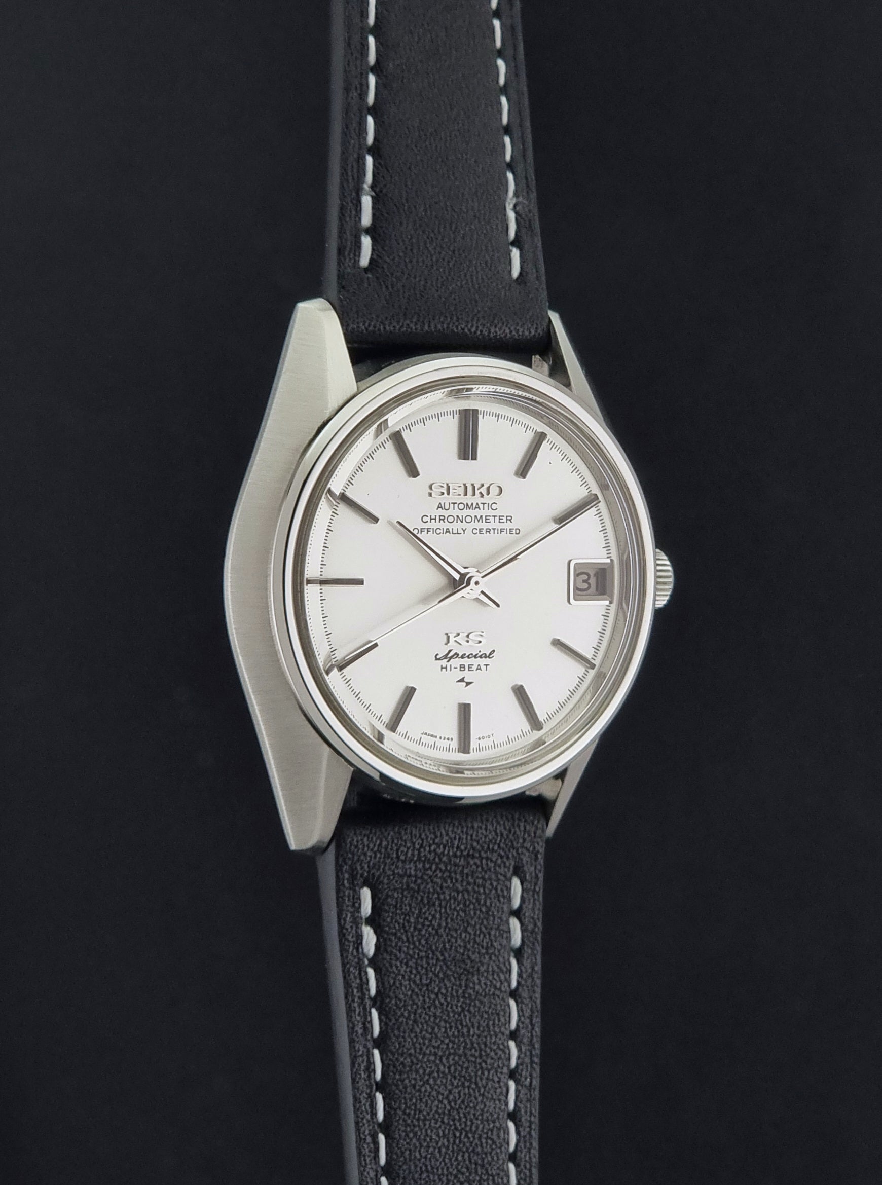 A Vintage King Seiko Special 5245-6010 Watch, white dial, and black leather strap with white stitching, photographed side profile against a dark background.