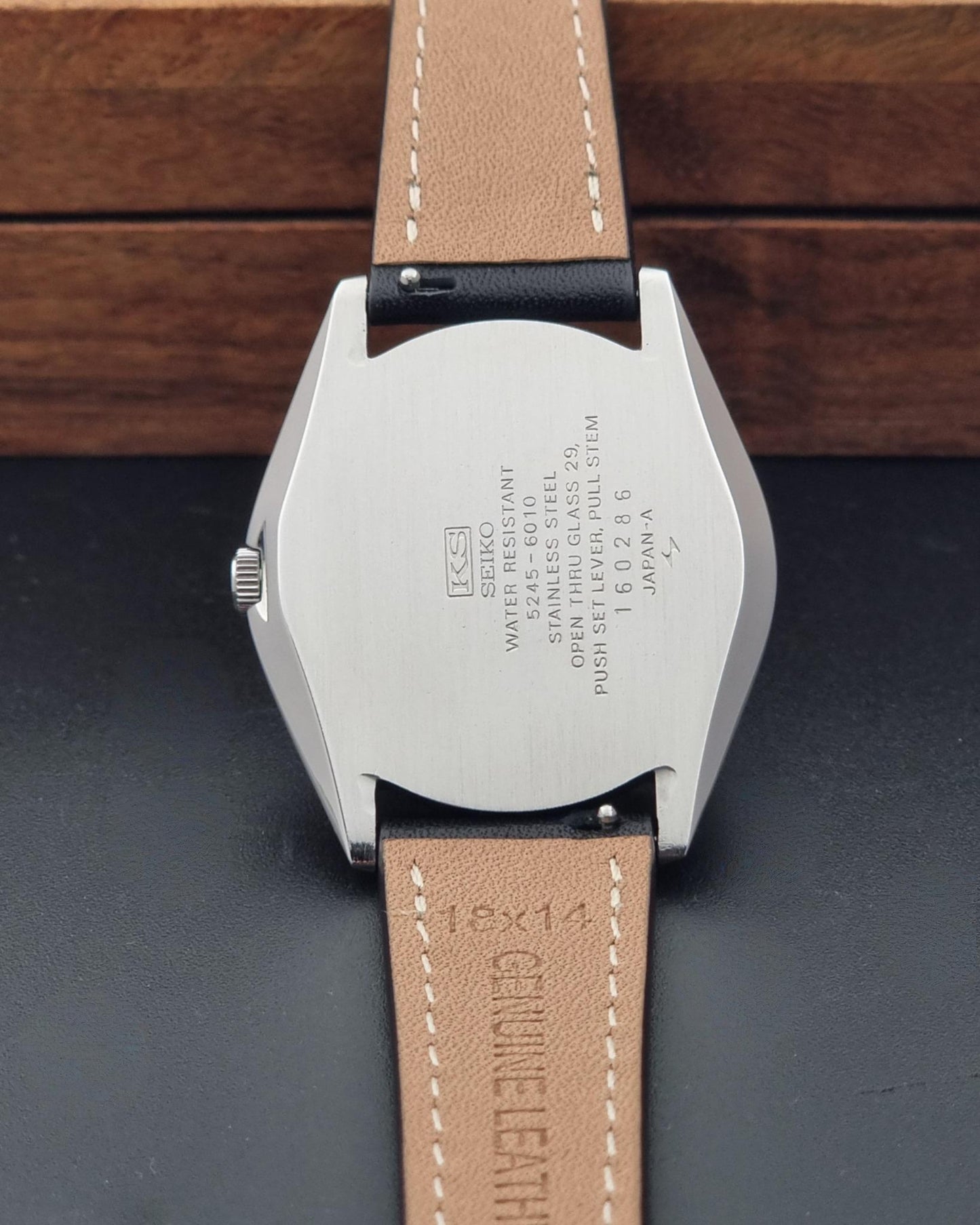 Close-up of the back of A Vintage King Seiko Special 5245-6010 Watch, photographed on a dark surface with a wooden box