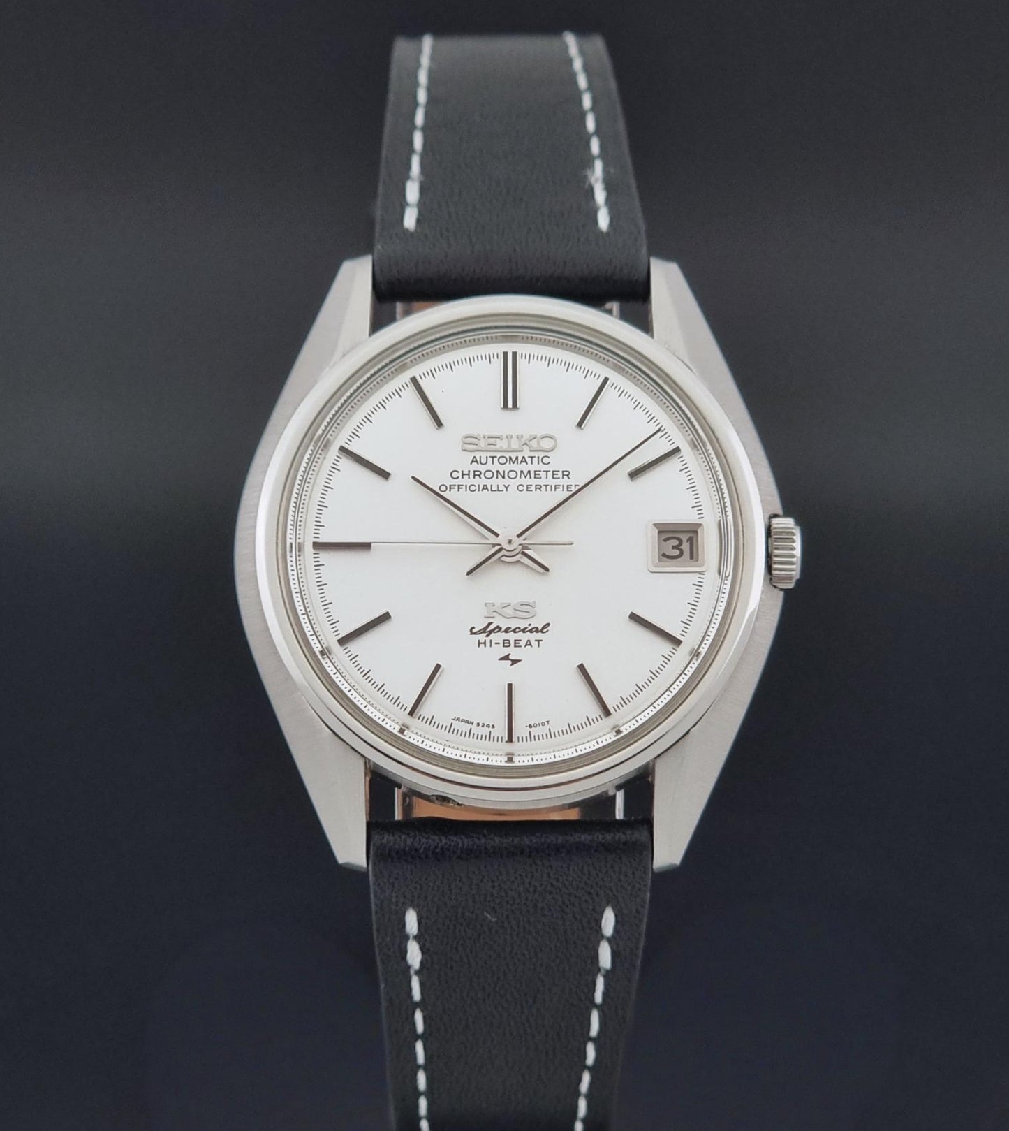 A Vintage King Seiko Special 5245-6010 Watch, white dial, and black leather strap with white stitching, photographed against a dark gray background
