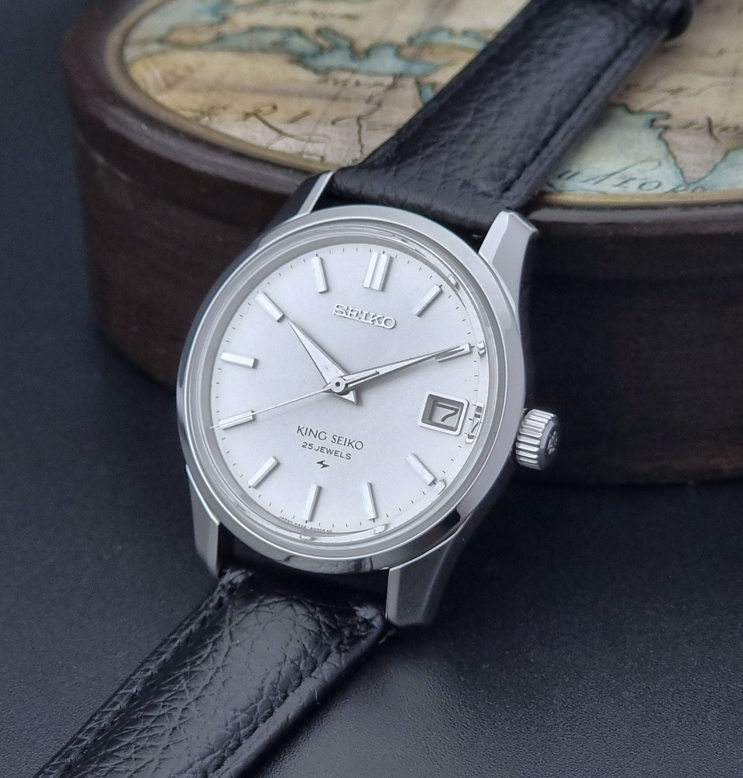 Vintage King Seiko Wristwatch with black leather strap on an old map background crown view