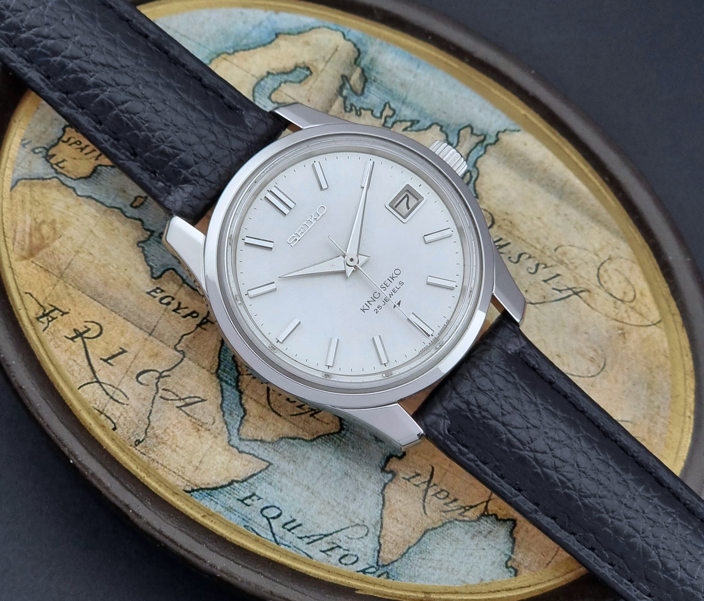 Vintage King Seiko Wristwatch with black leather strap on an old map background front view