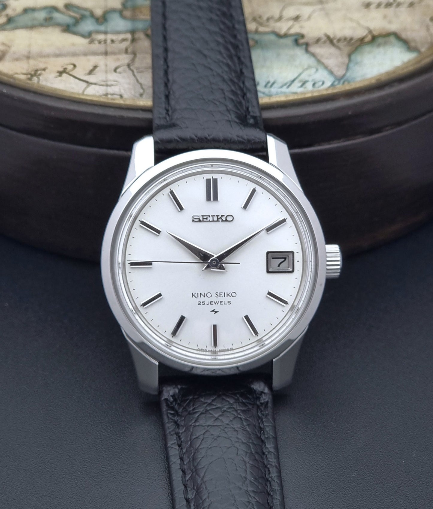 Vintage King Seiko Wristwatch with black leather strap on an old map background close front view