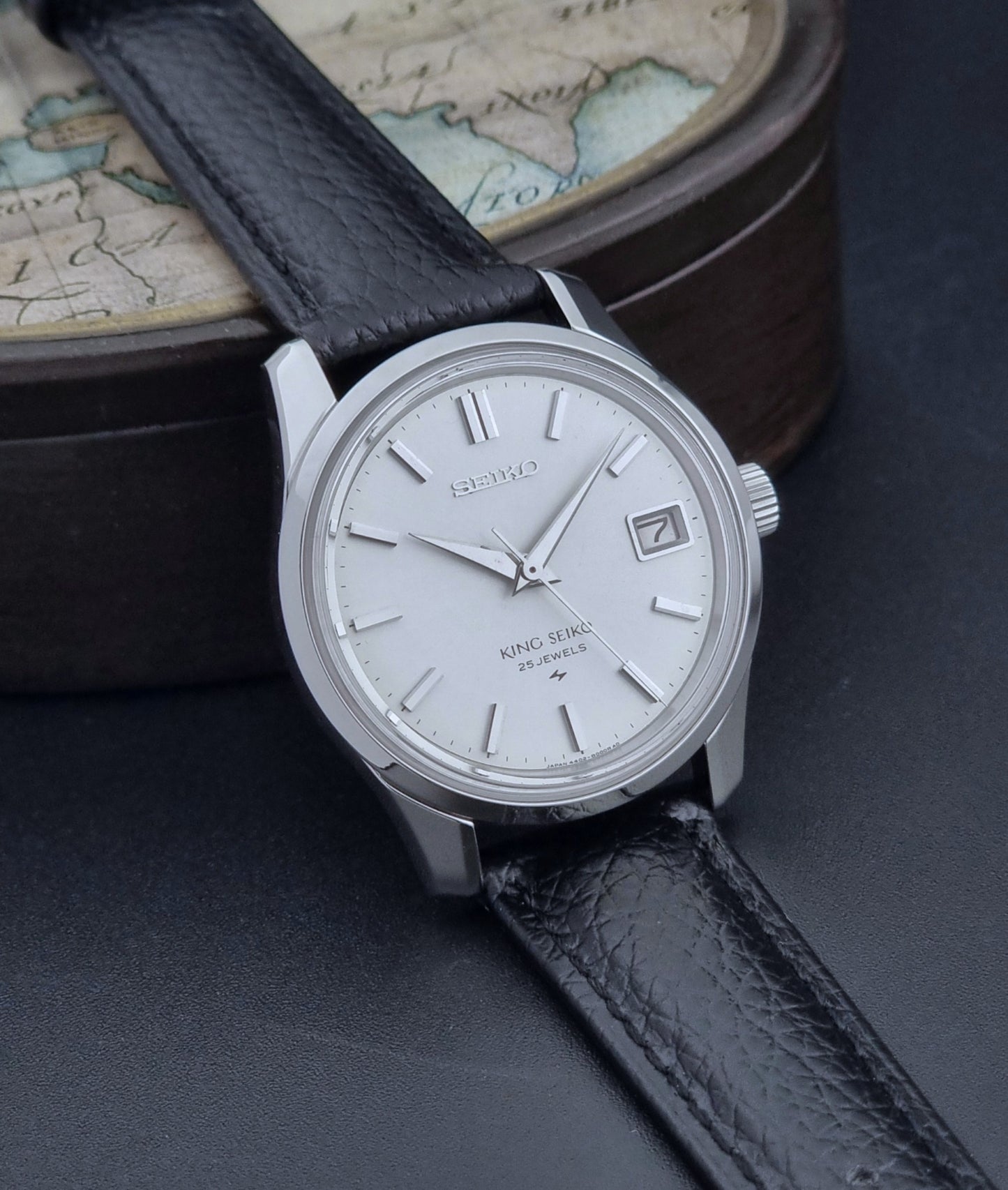 Vintage King Seiko Wristwatch with black leather strap on an old map background side view