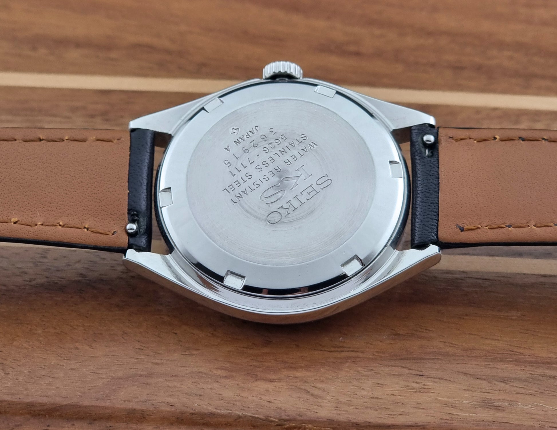 Vintage King Seiko Wristwatch with black leather strap and silver case on a wooden surface case back view