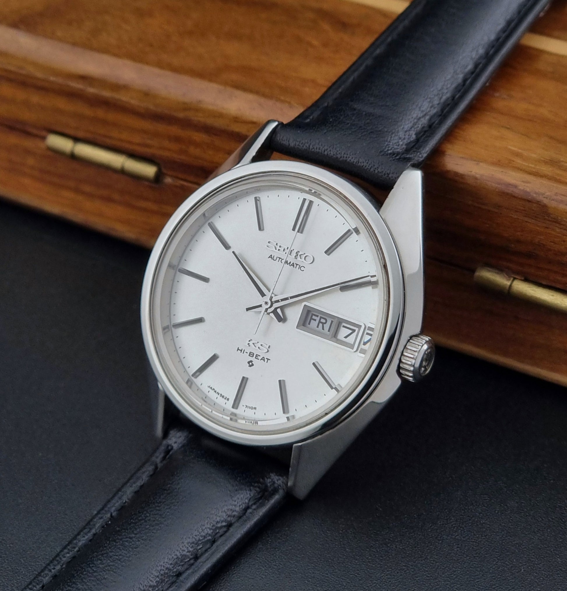 Vintage King Seiko Wristwatch with black leather strap and silver case on a wooden surface crown view